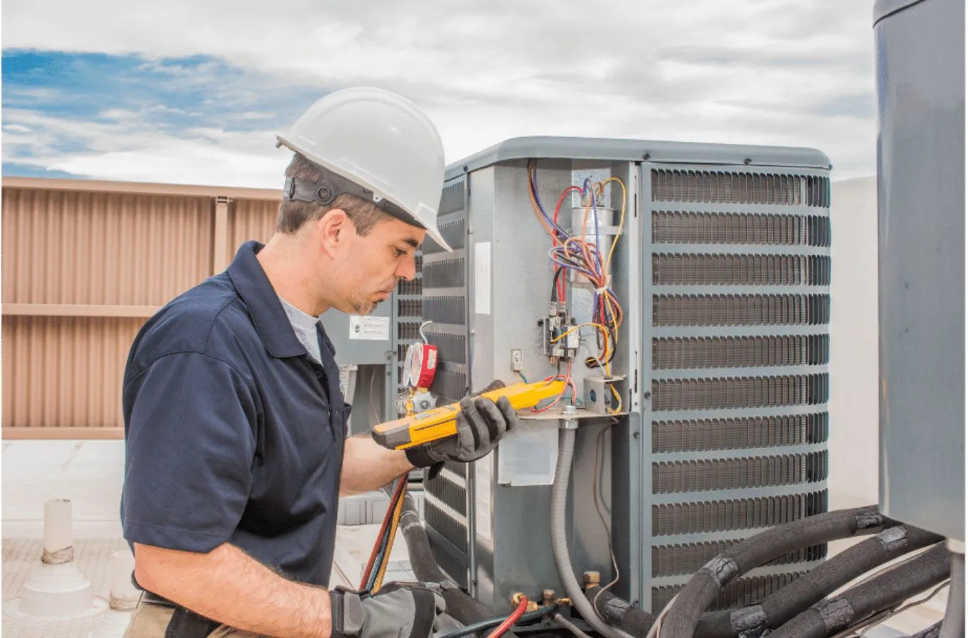 HVAC technician in a hard hat testing a rooftop condenser's electrical panel during HVAC service in Tampa, FL.