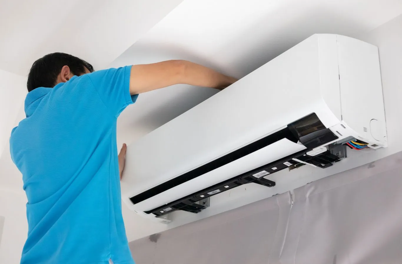 HVAC technician opening the front panel of a wall-mounted indoor AC unit during an AC tune-up and inspection for a Venice, FL home.