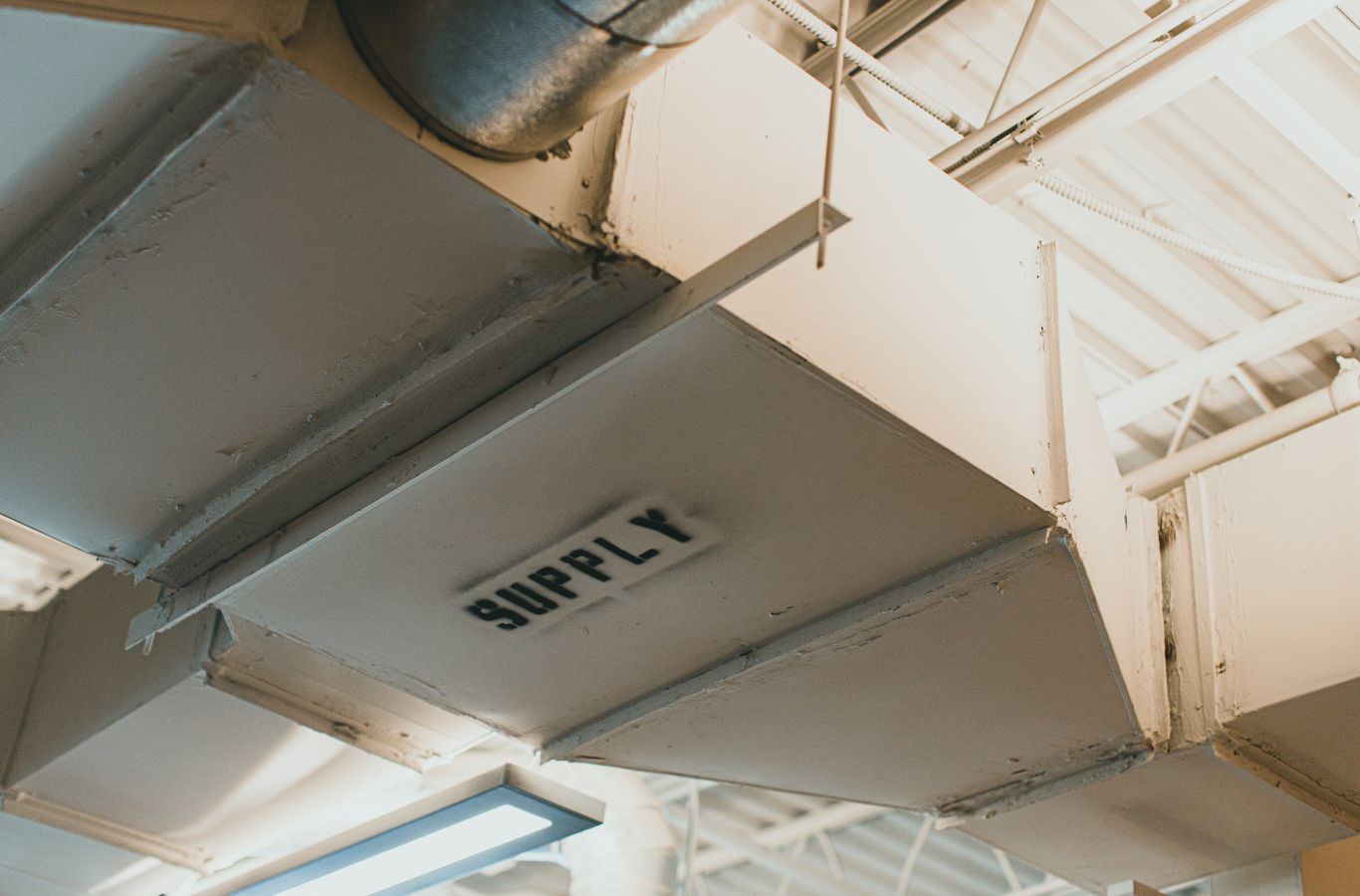 Overhead supply duct trunk labeled SUPPLY beneath a ceiling. Air Duct Cleaning Near Me.