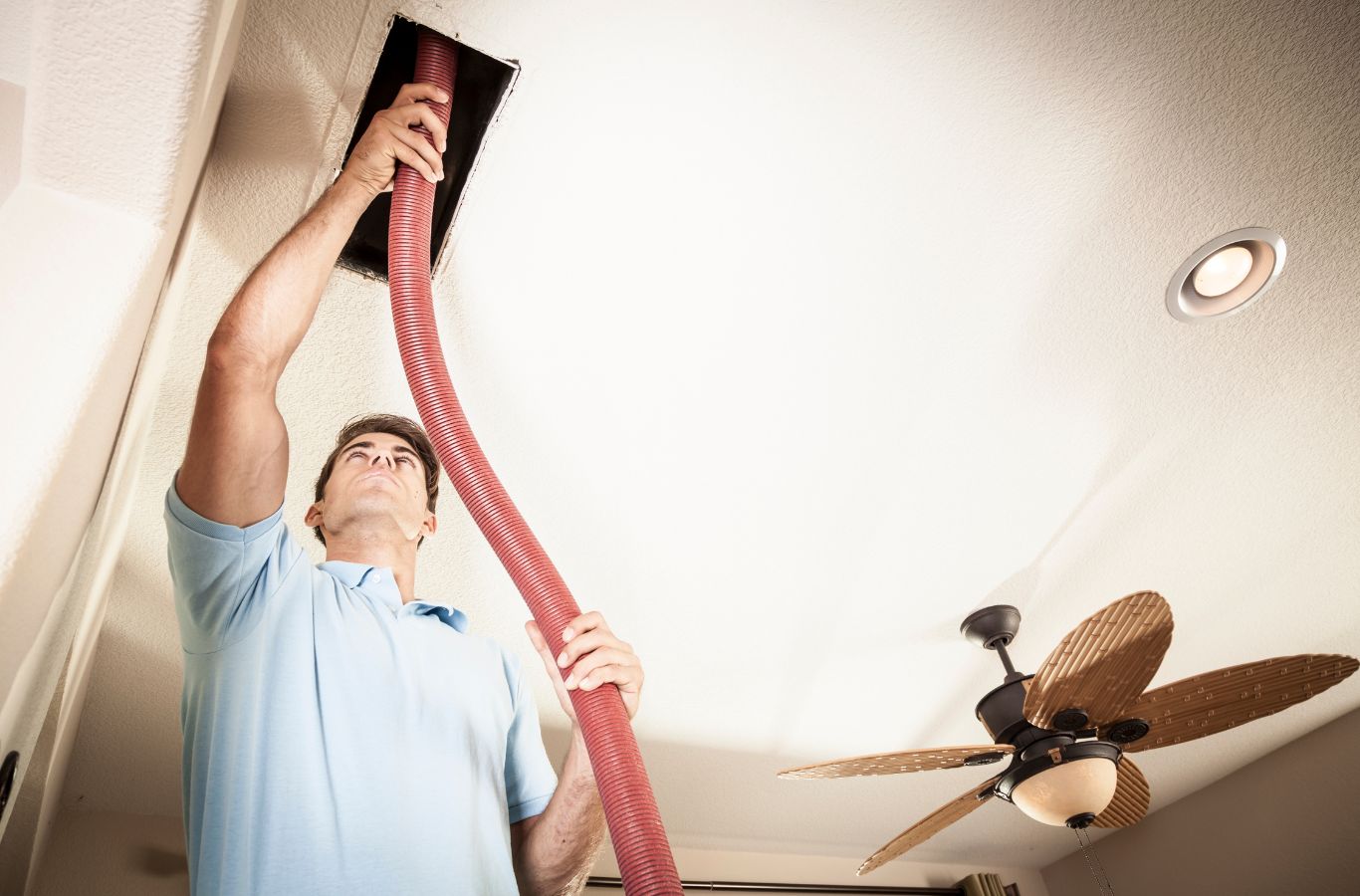 Technician guiding a red vacuum hose into a ceiling vent during air duct cleaning in a Bradenton, FL home.