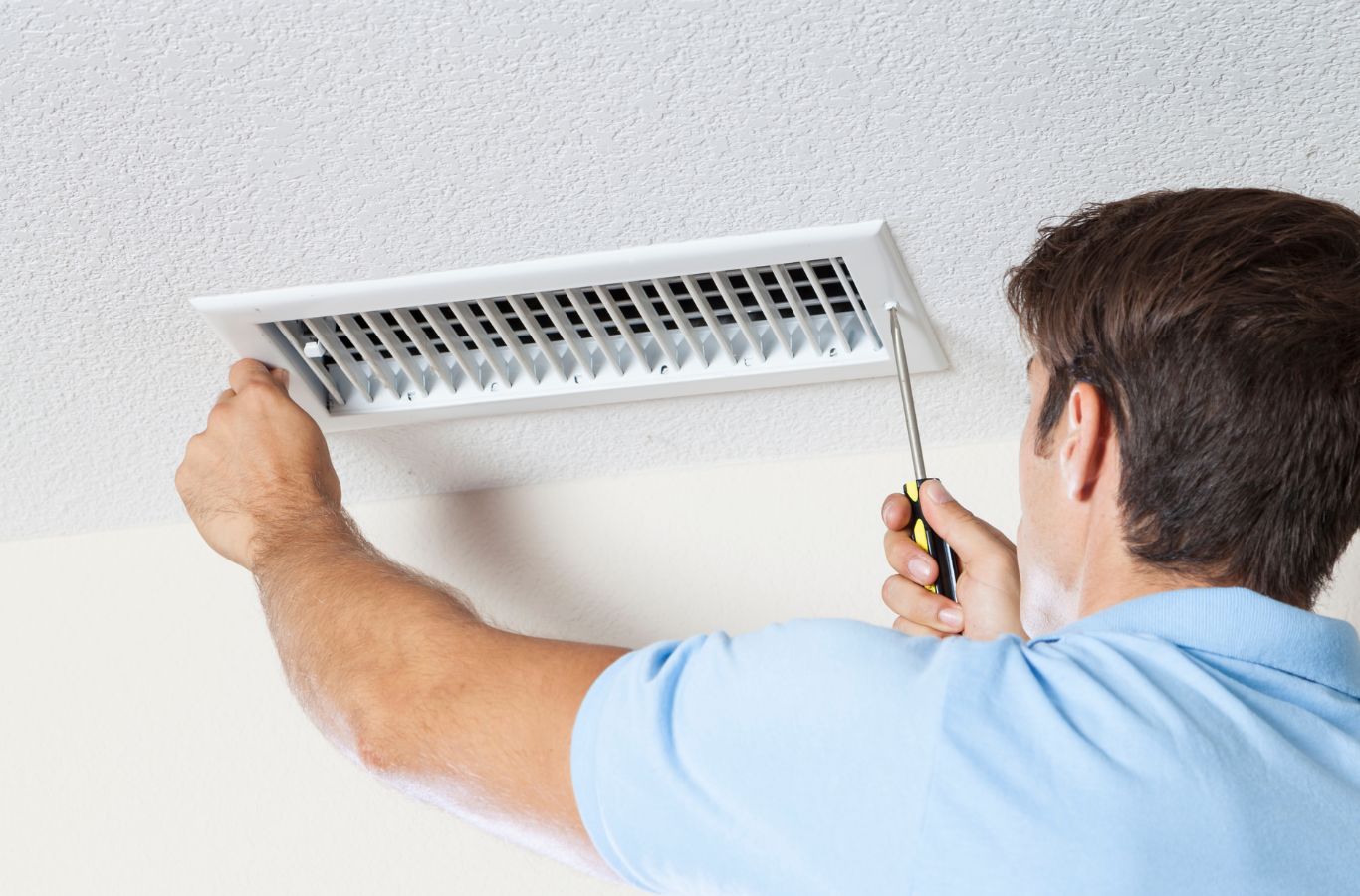 Technician unscrewing a ceiling register grille to access the duct behind it. Air Duct Cleaning Near Me.