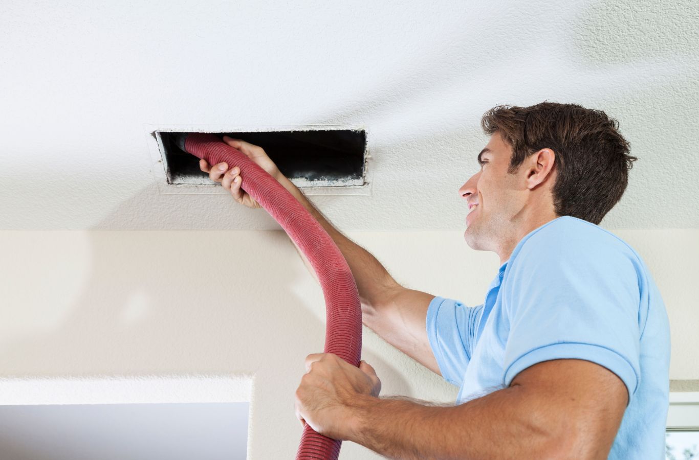 Technician feeding a red vacuum hose into a ceiling supply vent during air duct cleaning in a Palmetto, FL home.