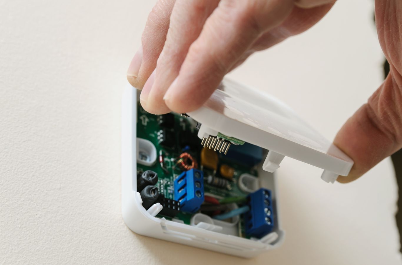 Hand clipping the front cover onto a wall-mounted thermostat base. Thermostat Installation & Repair Near Me.