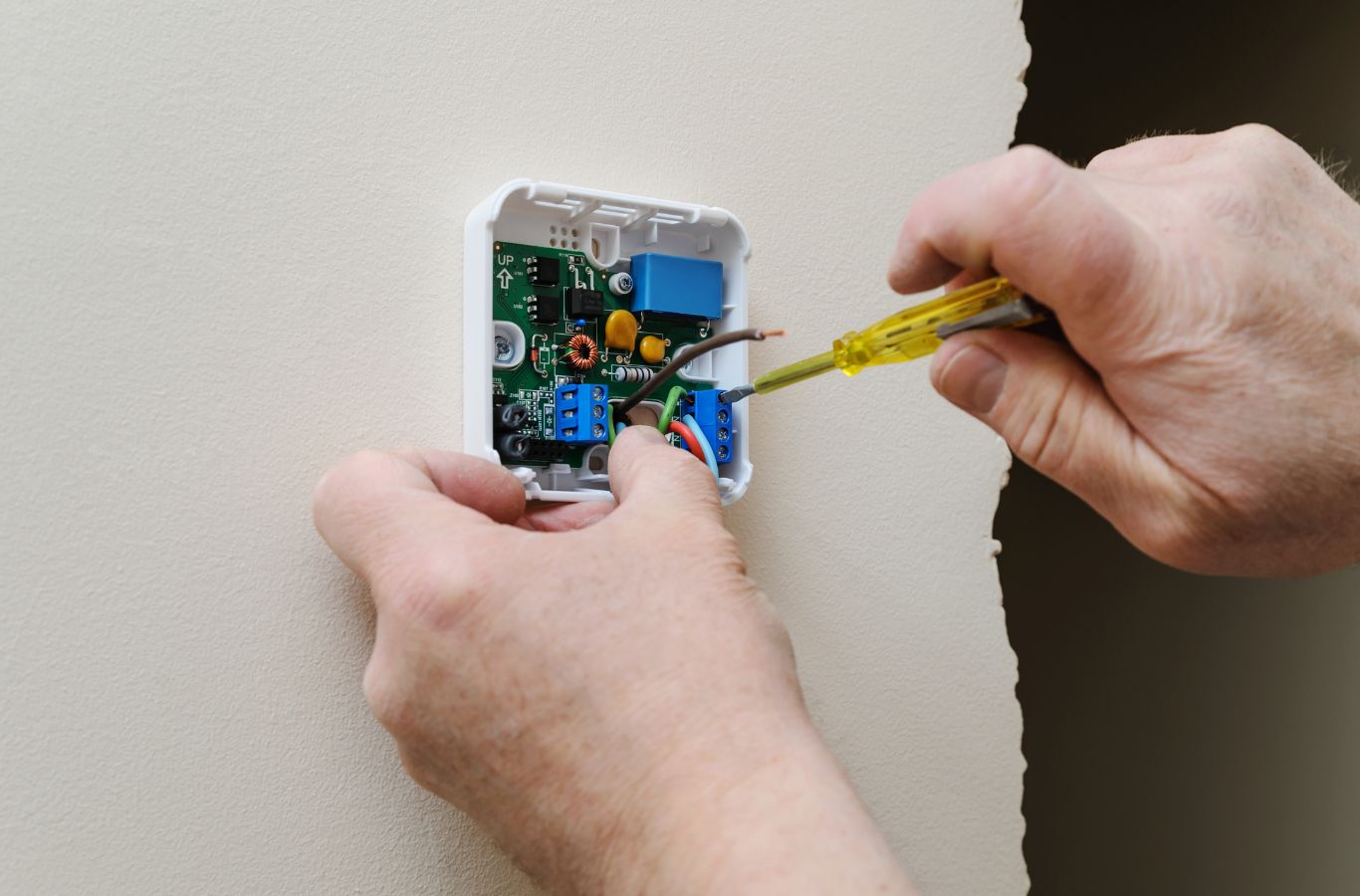 Screwdriver tightening wire terminals on an open thermostat base. Thermostat Installation & Repair Near Me.