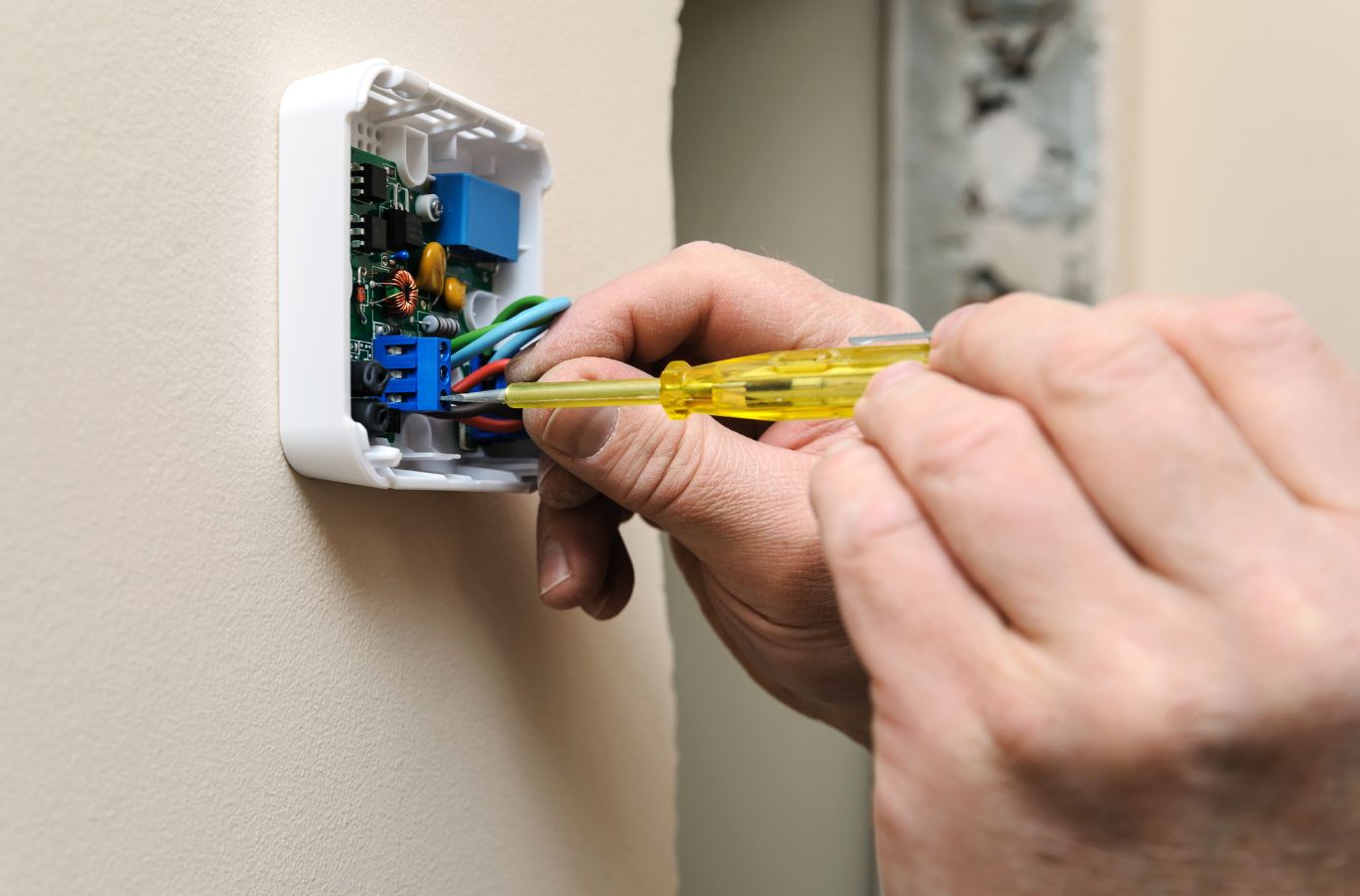 Screwdriver securing wires in the terminal block of a wall thermostat base. Thermostat Installation & Repair Near Me.