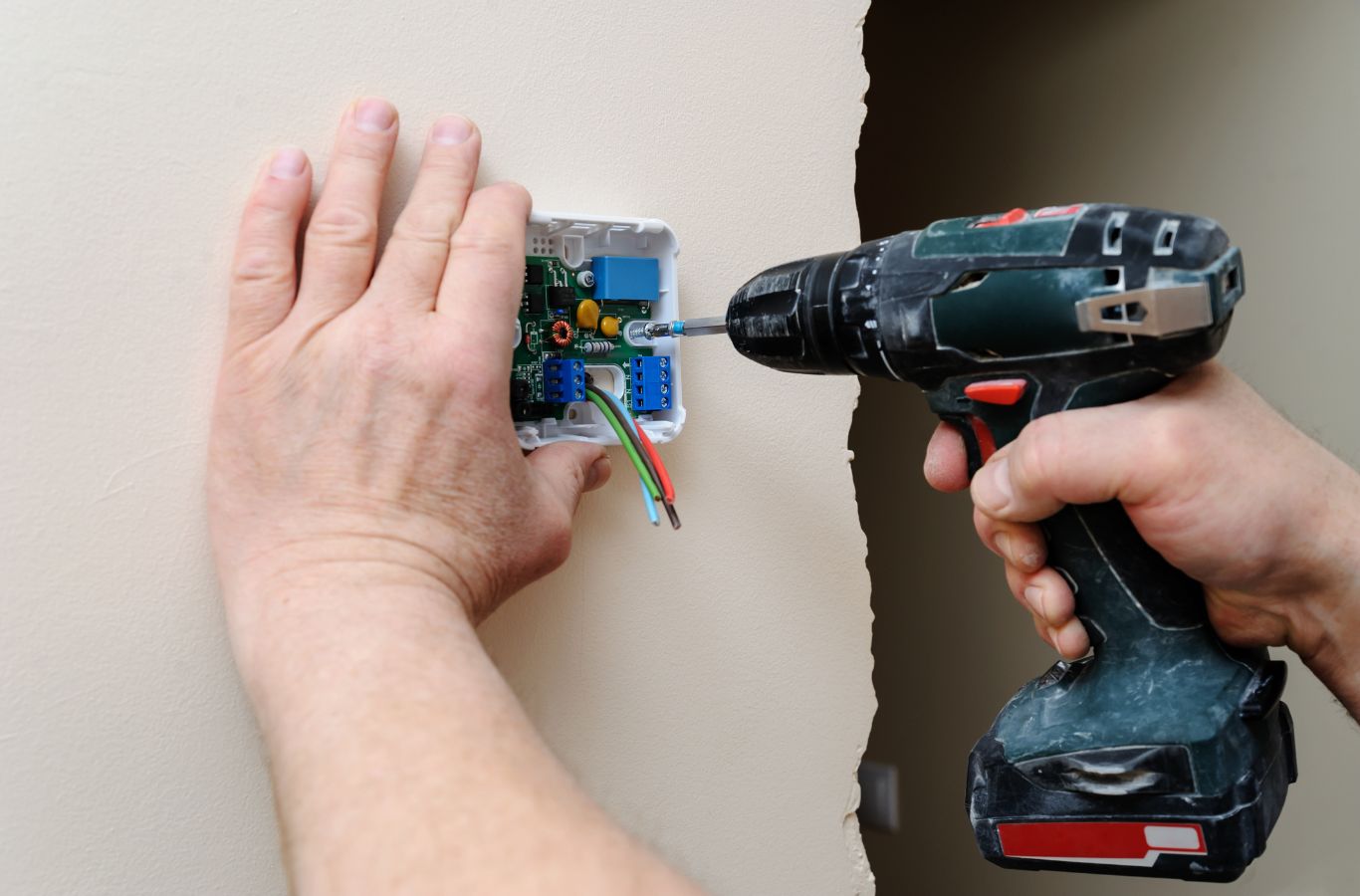Hand holding a thermostat base against the wall while a drill secures it during thermostat installation in a Lakewood Ranch, FL home.