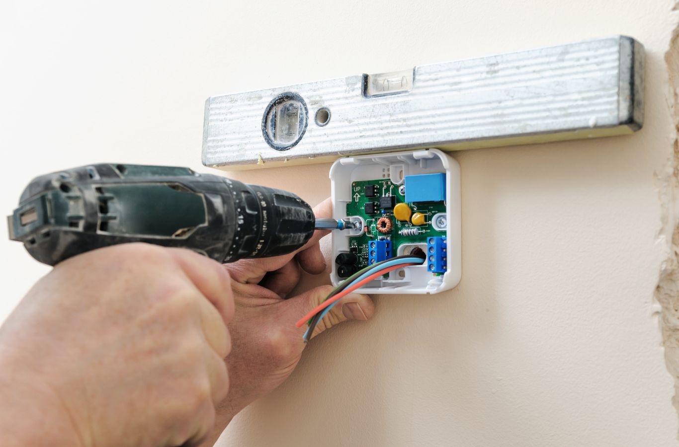 Drill fixing a thermostat base to the wall beneath a spirit level during thermostat installation in a Longboat Key, FL home.