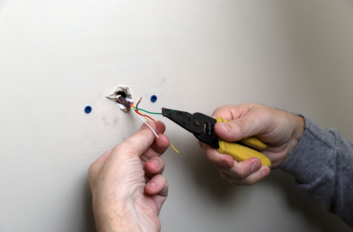 Wire strippers preparing thermostat wires at a wall opening during thermostat installation in a Siesta Key, FL home.