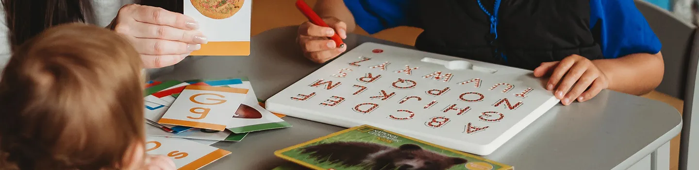 Close-up of therapist’s hands guiding a child’s hands during a speech therapy session, inviting you to book a free consultation.