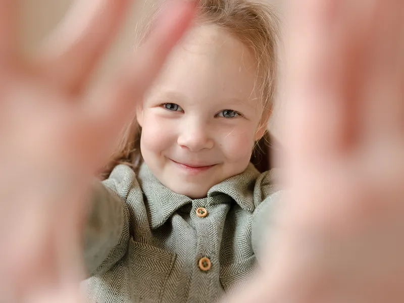 Child playfully looking through their hands, highlighting a joyful and welcoming environment at Speech and Language Nook.