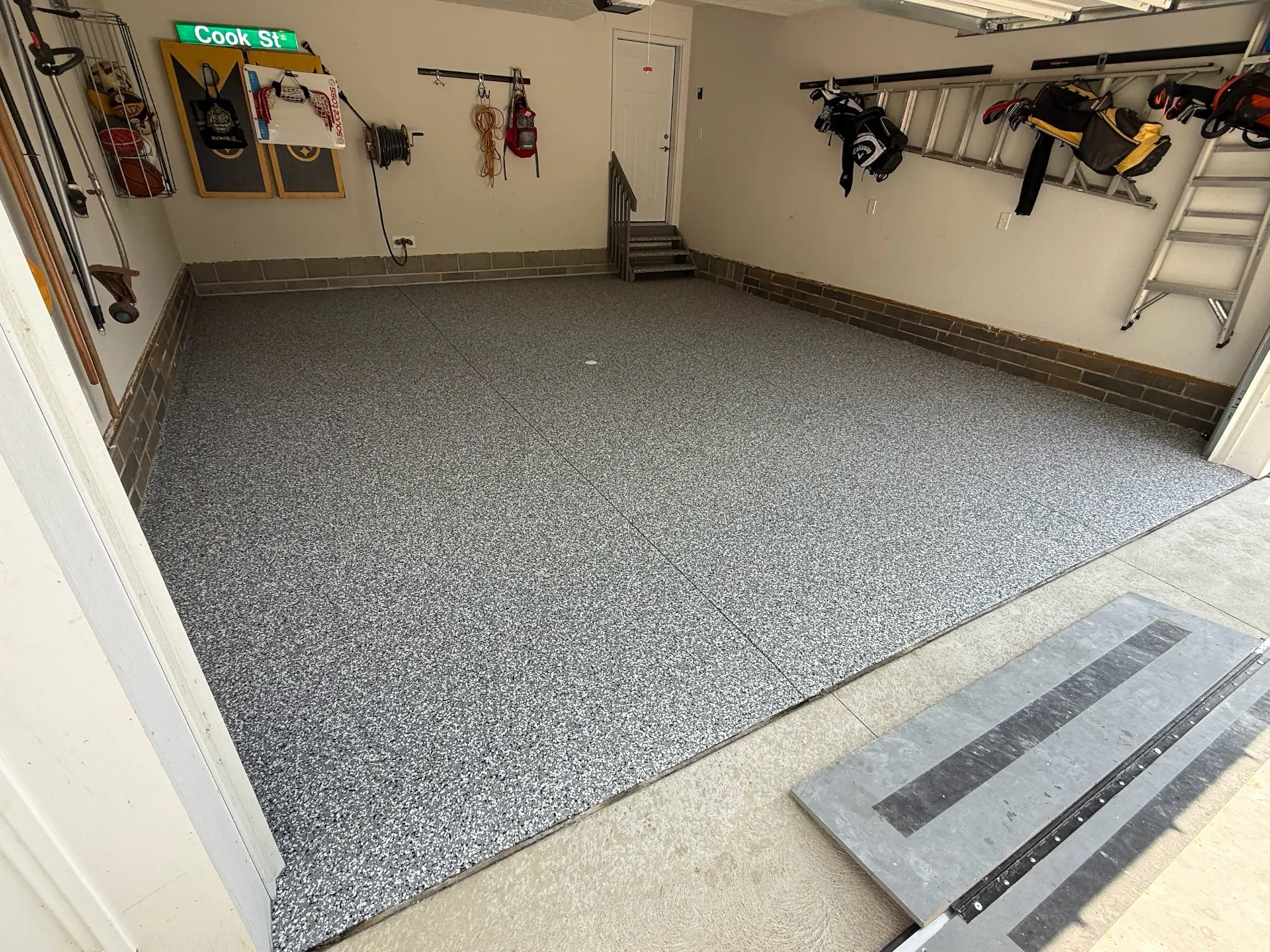Gray flake polyaspartic garage floor with clean edges at the threshold and organized wall racks.
