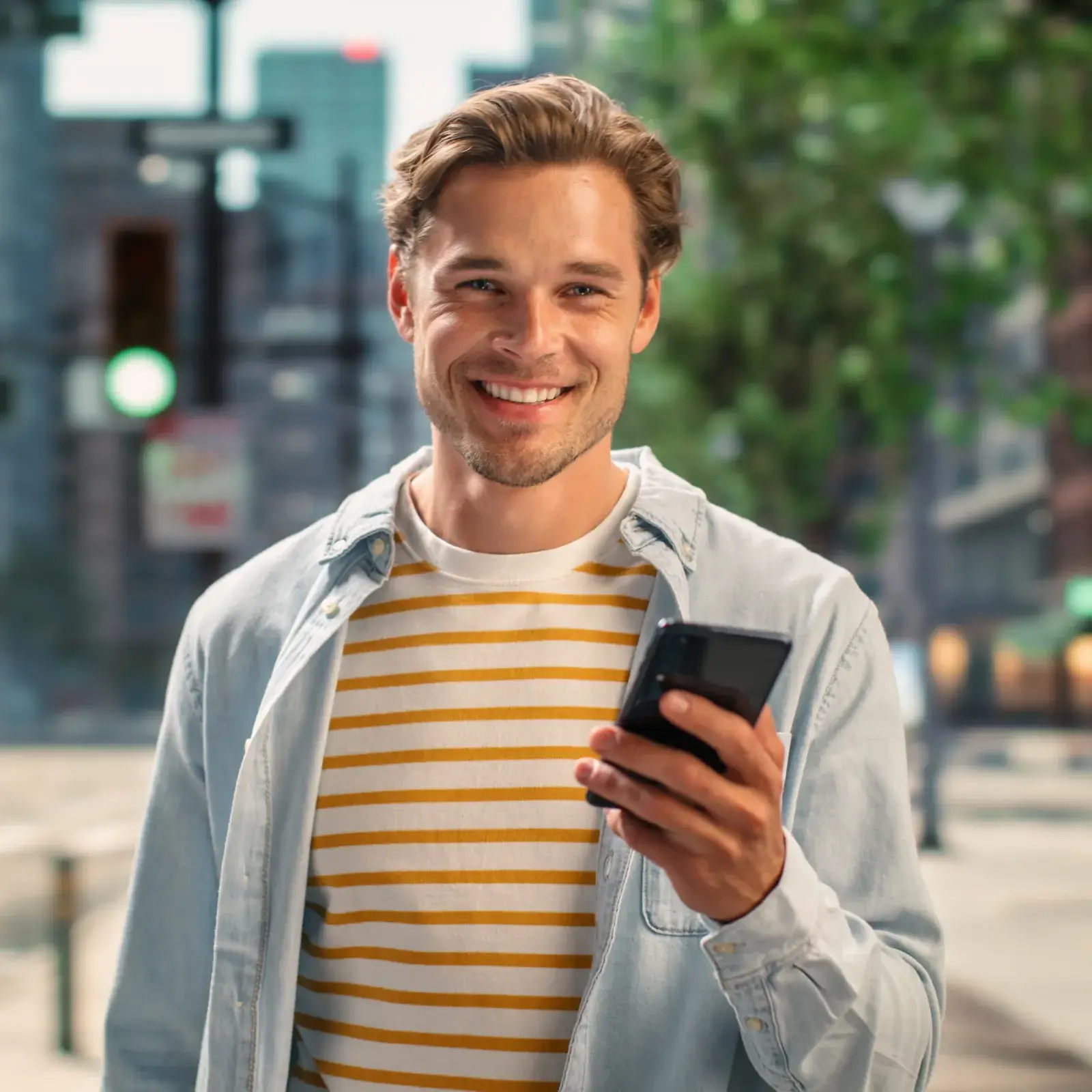 A person smiles while holding a smartphone on a city street during the day.