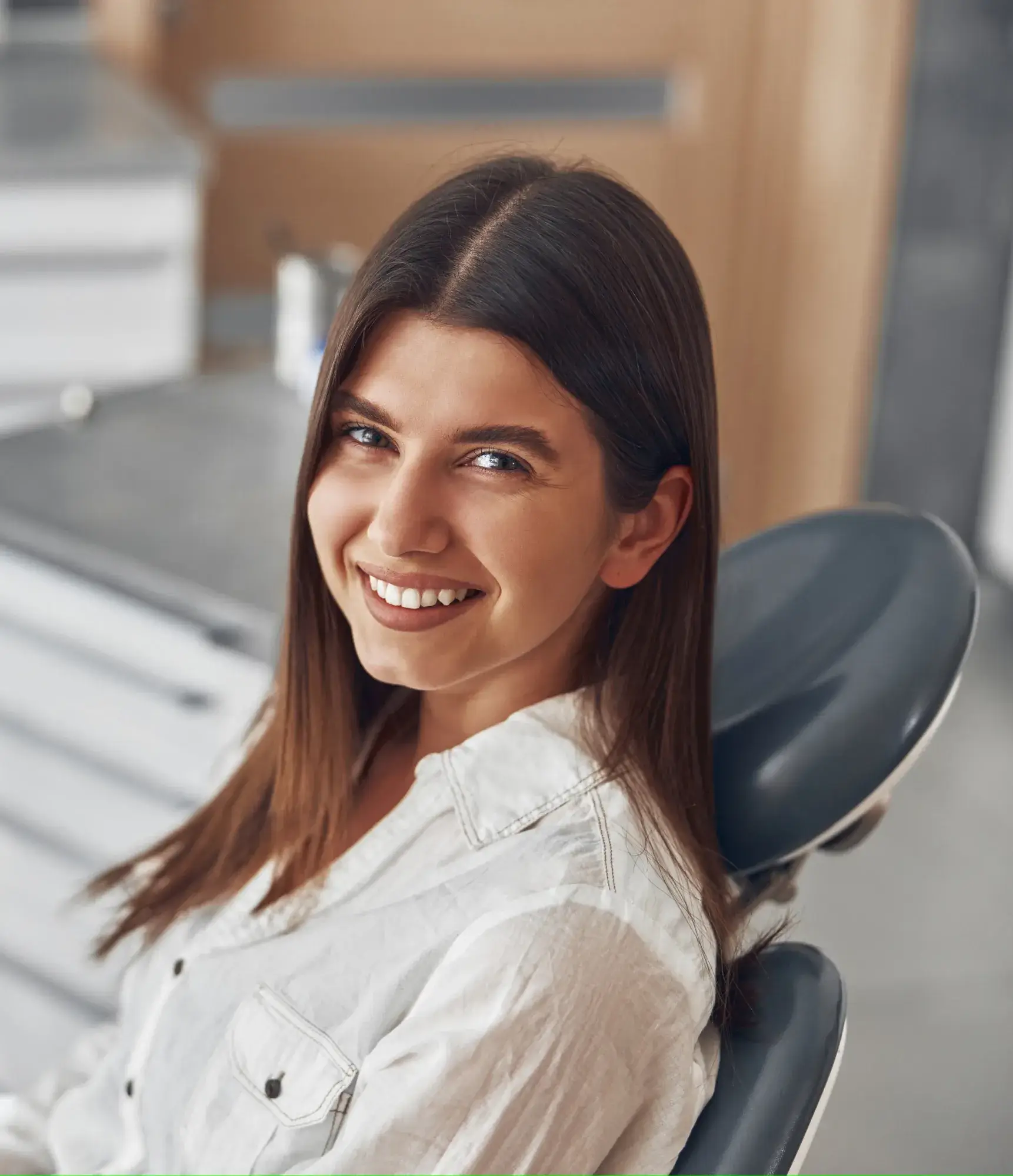 A woman in a dental chair smiles at the camera, wearing a white shirt.