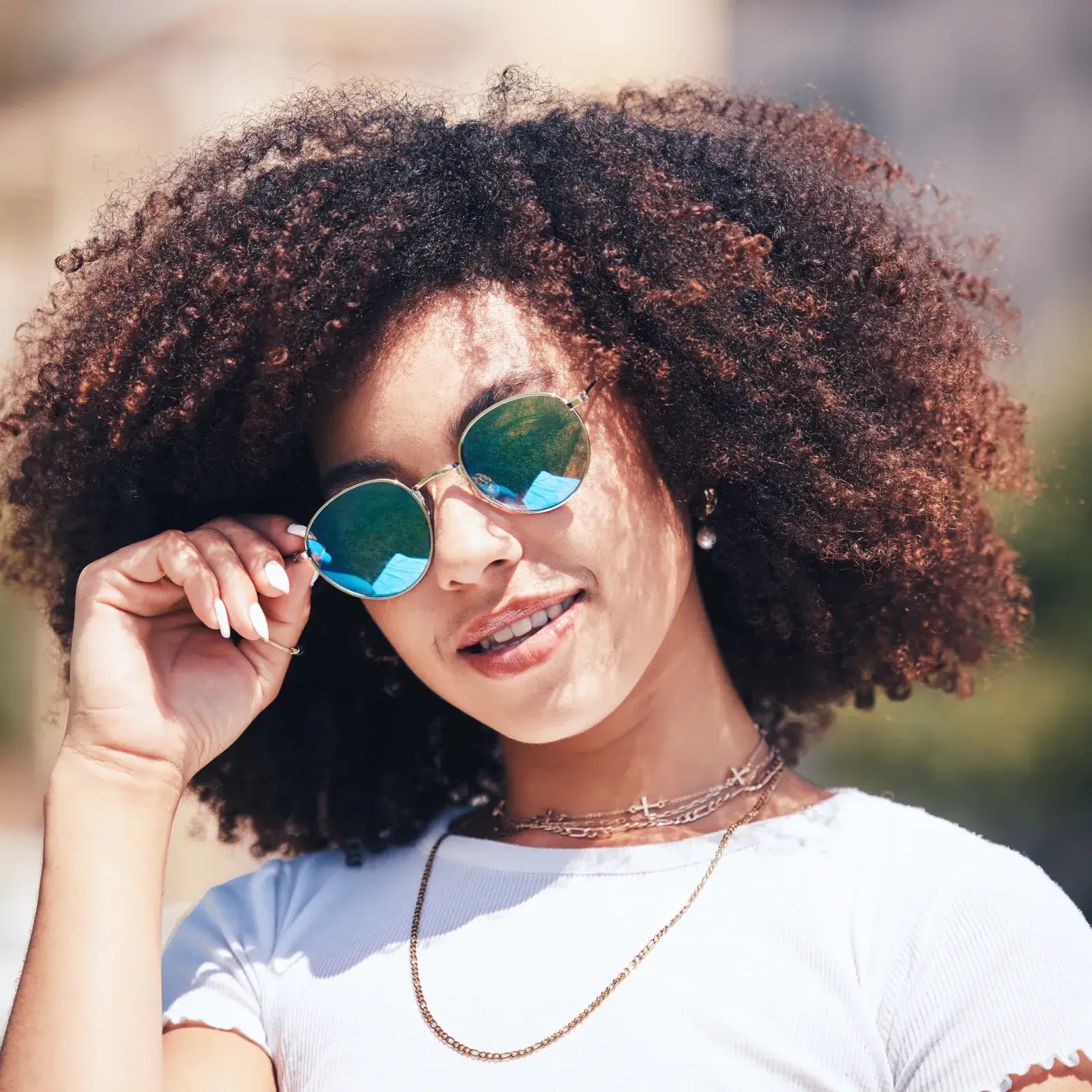 A person with curly hair and sunglasses smiles at the camera.