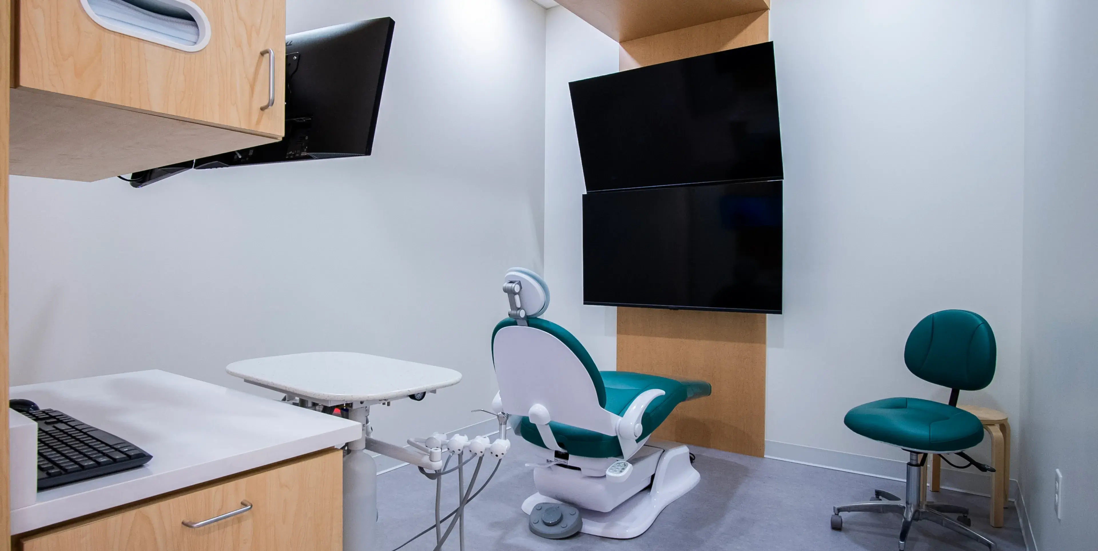 Dental office with a chair, exam light, and monitors on the wall.