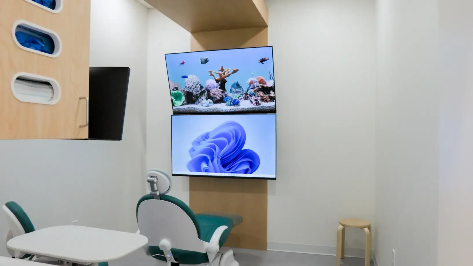 A dental exam room with a dentist chair facing two screens displaying ocean and digital images.