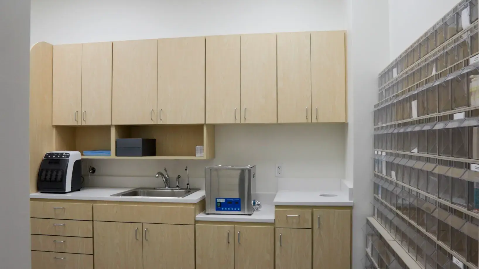 A small laboratory with light wood cabinets, a sink, and equipment on the countertop.