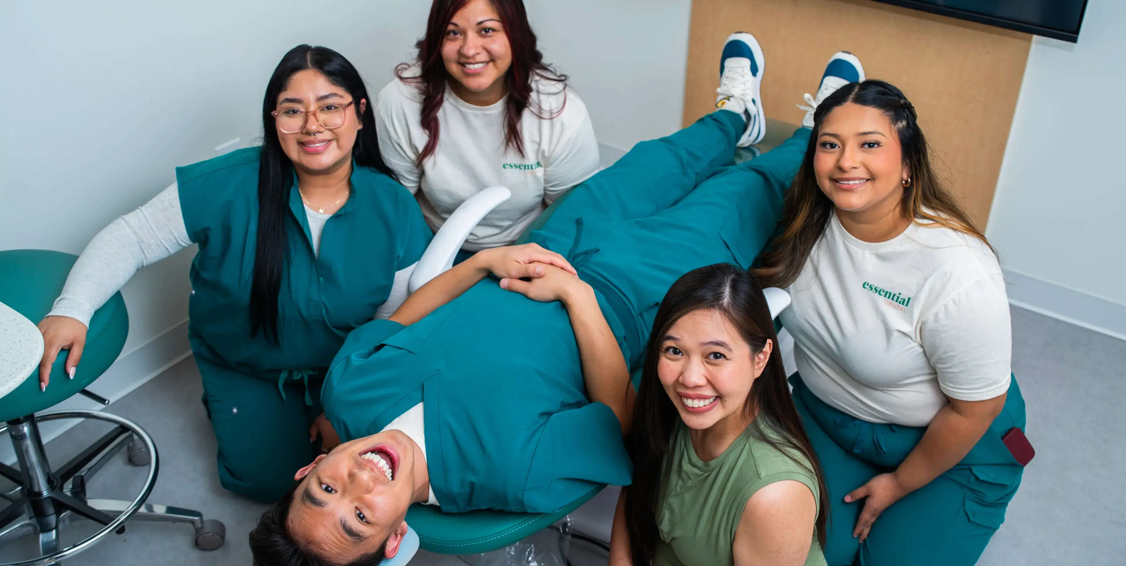 A smiling group of five people, one lying on chairs, pose together in a medical setting.