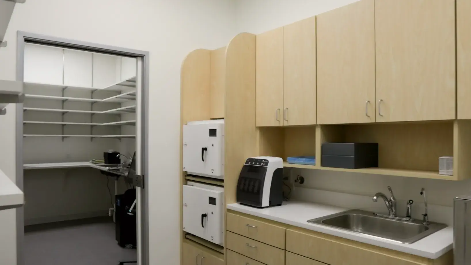 A small kitchen area with a sink, cabinets, and a doorway leading to a storage room.
