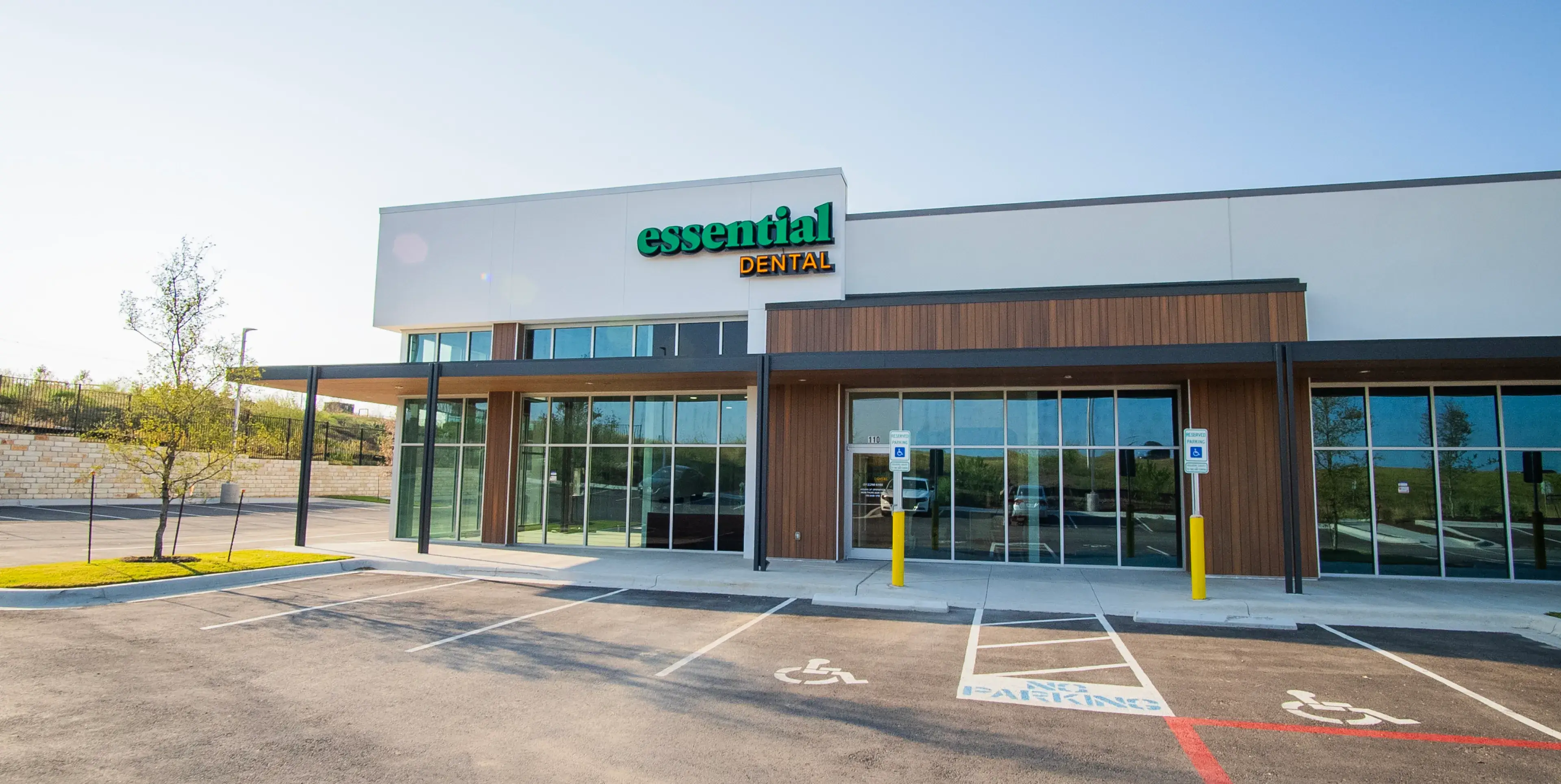 A dental office with a sign reading "Essential Dental" on a sunny day in a parking lot.