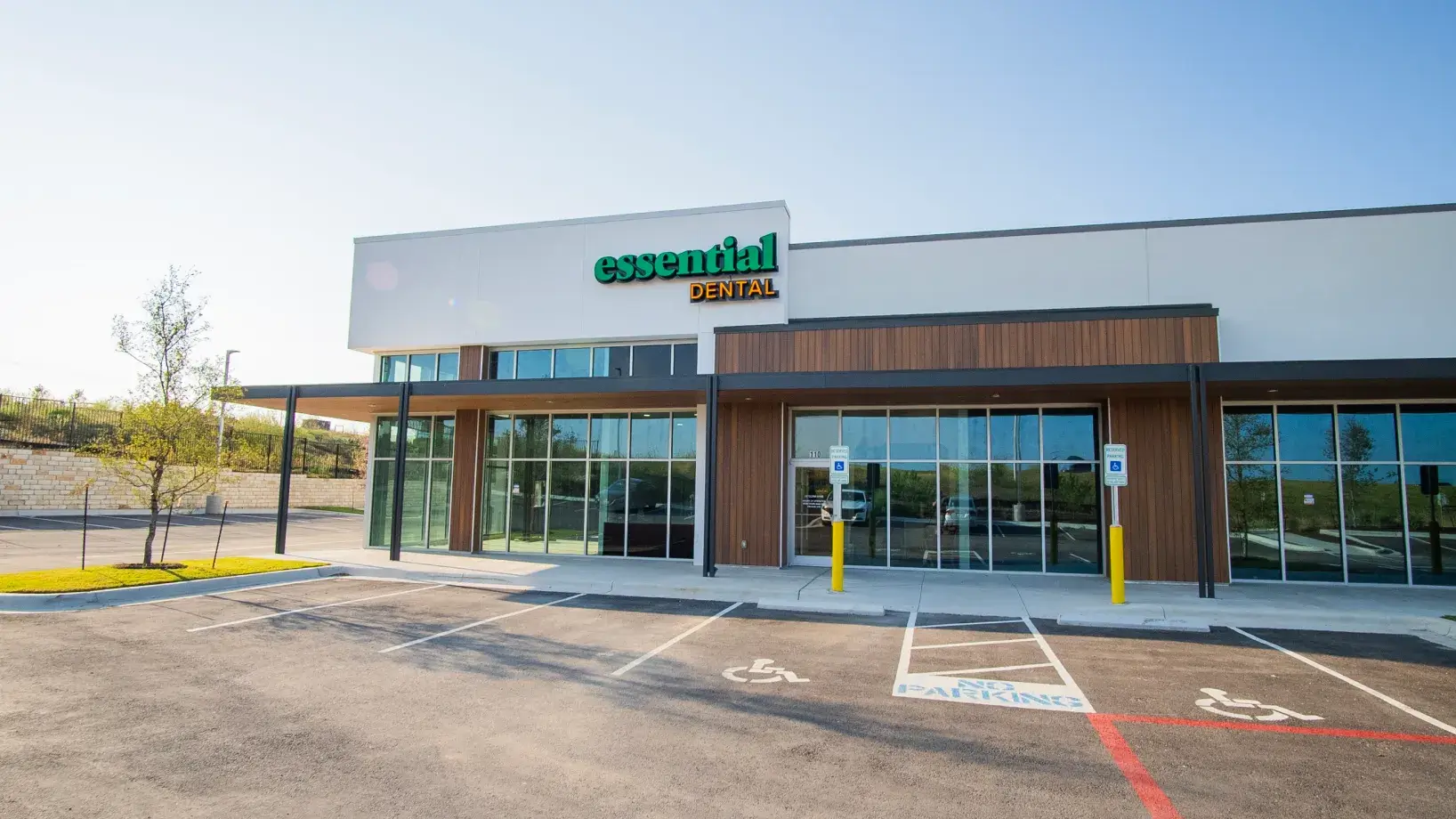 Exterior view of a dental clinic building with glass doors and designated parking spaces in front.