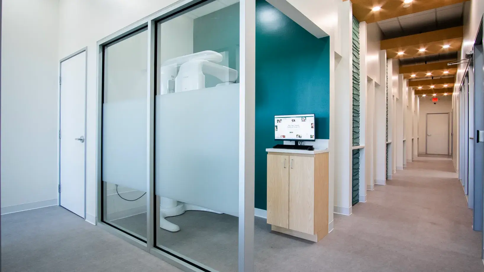 A dental office hallway with a digital X-ray machine and a computer on a wooden stand.