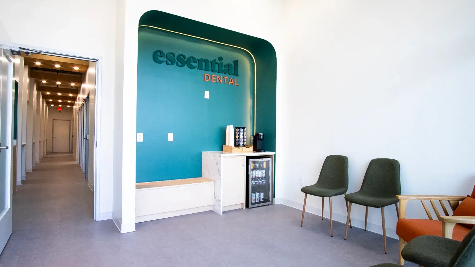 Dental office waiting area with three chairs, a mini fridge, and essential dental sign on the wall.