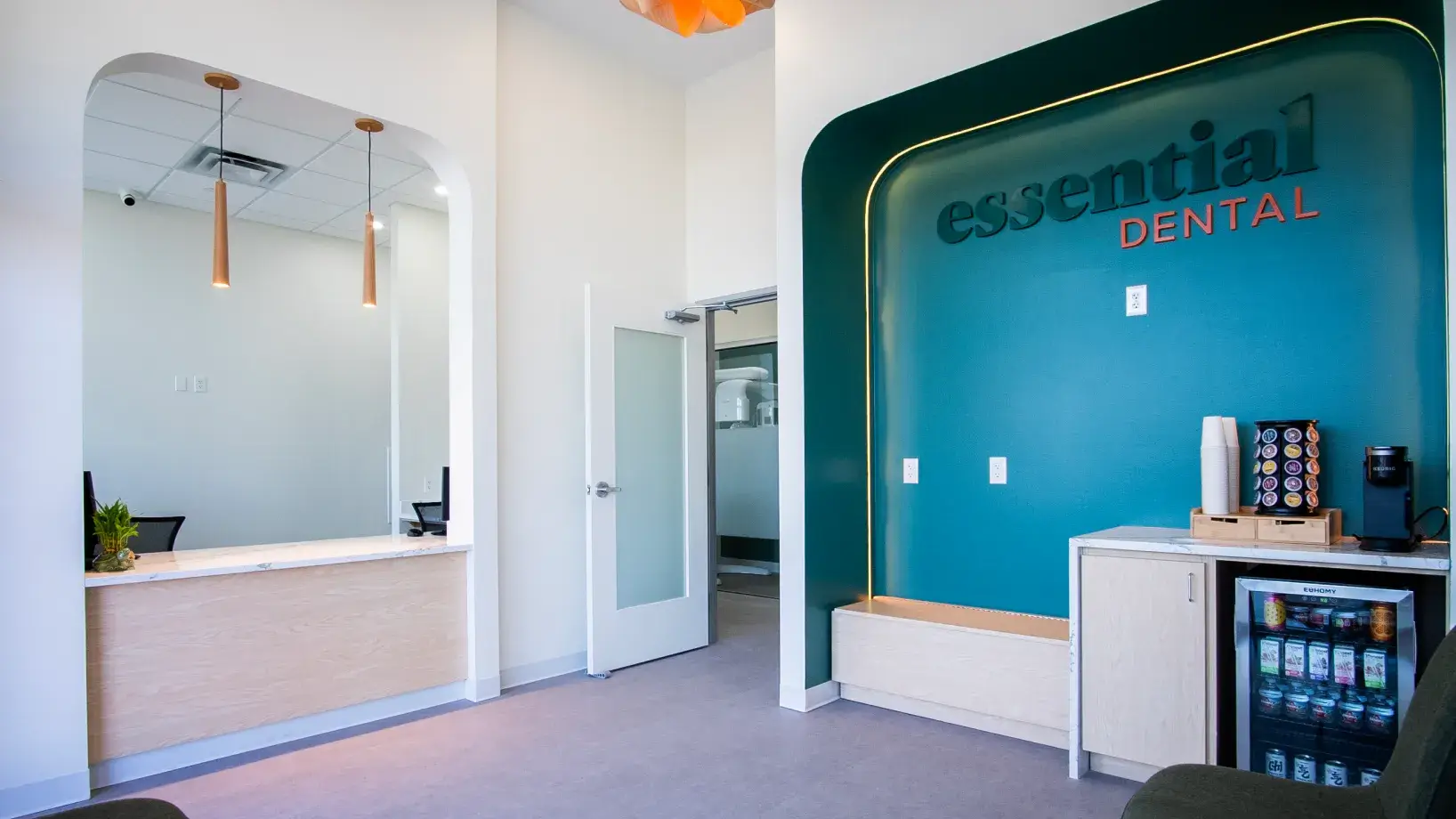 Dental office reception area with a "Essential Dental" sign, counter, and refreshments station.