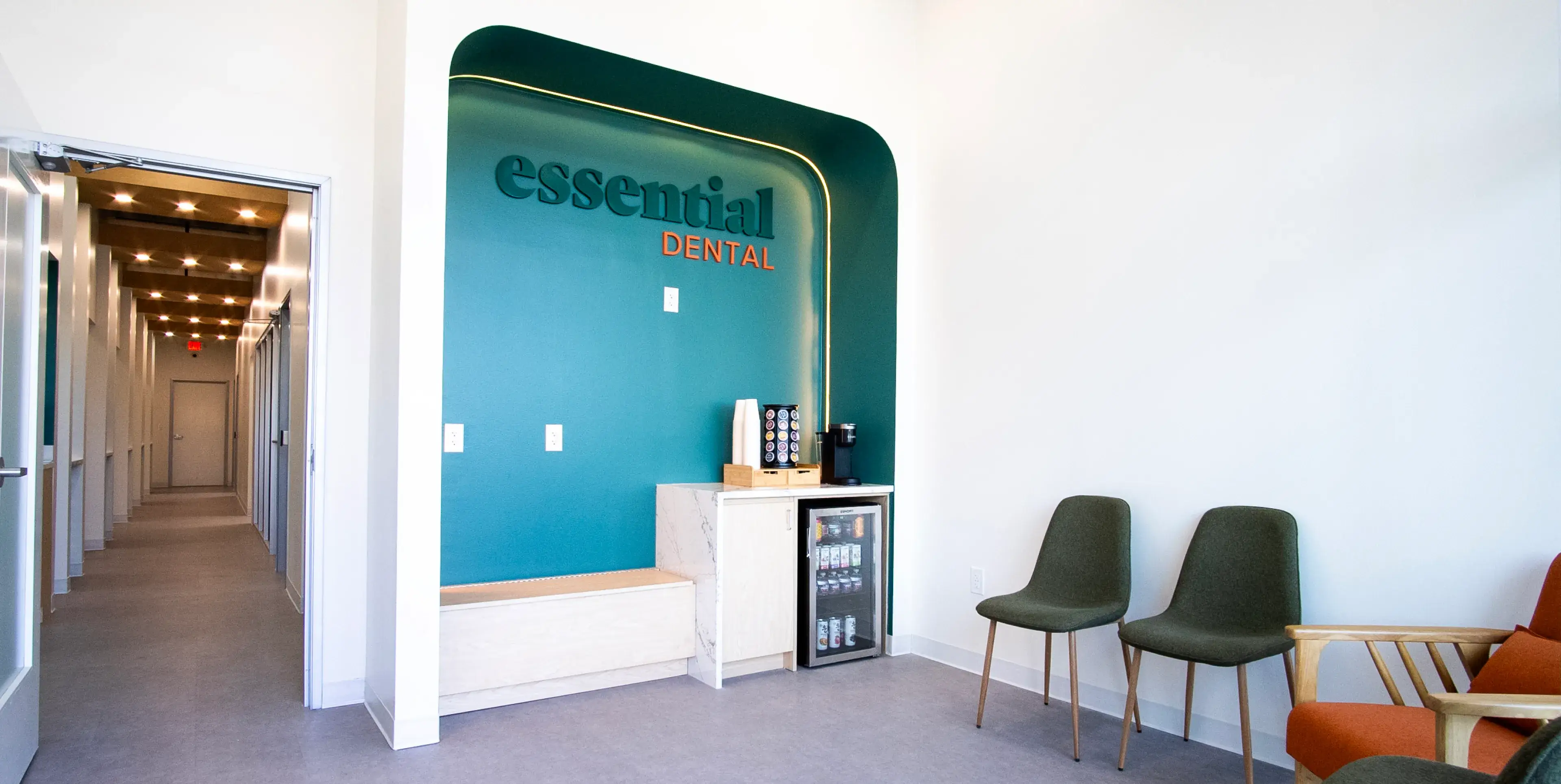 Dental office waiting area with two green chairs, a coffee station, and a sign reading "Essential Dental."