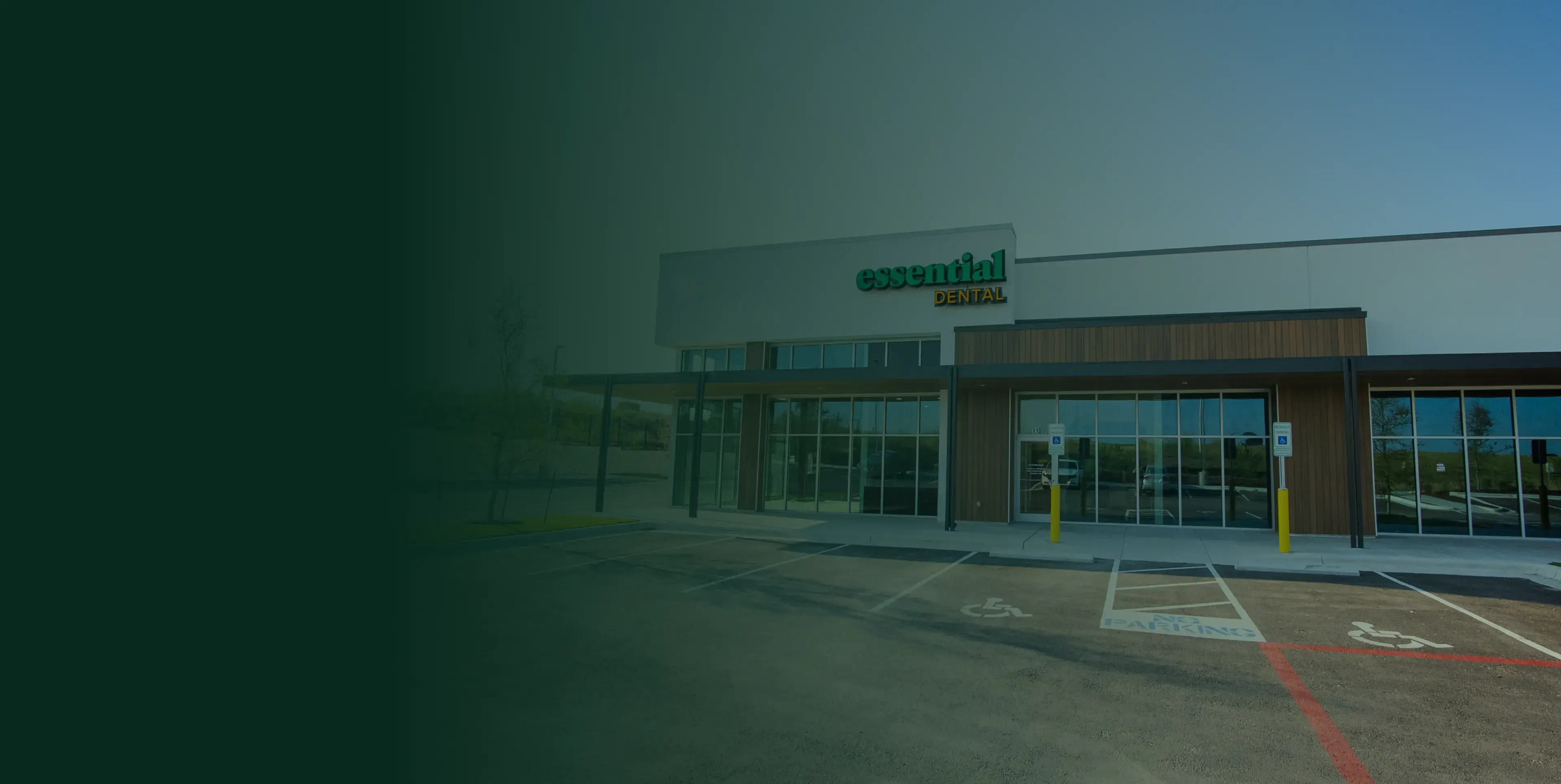 Exterior of Essential Dental building with large glass windows and a parking area in front.