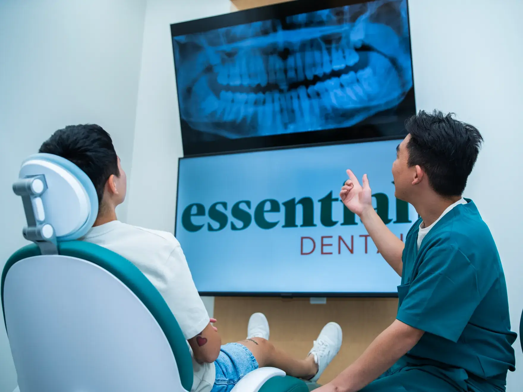 Dentist in scrubs discusses dental X-ray with patient sitting in a chair.