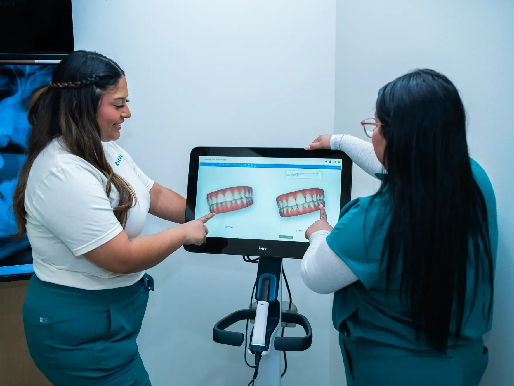 Two dental professionals discuss teeth images on a computer screen in a clinic setting.