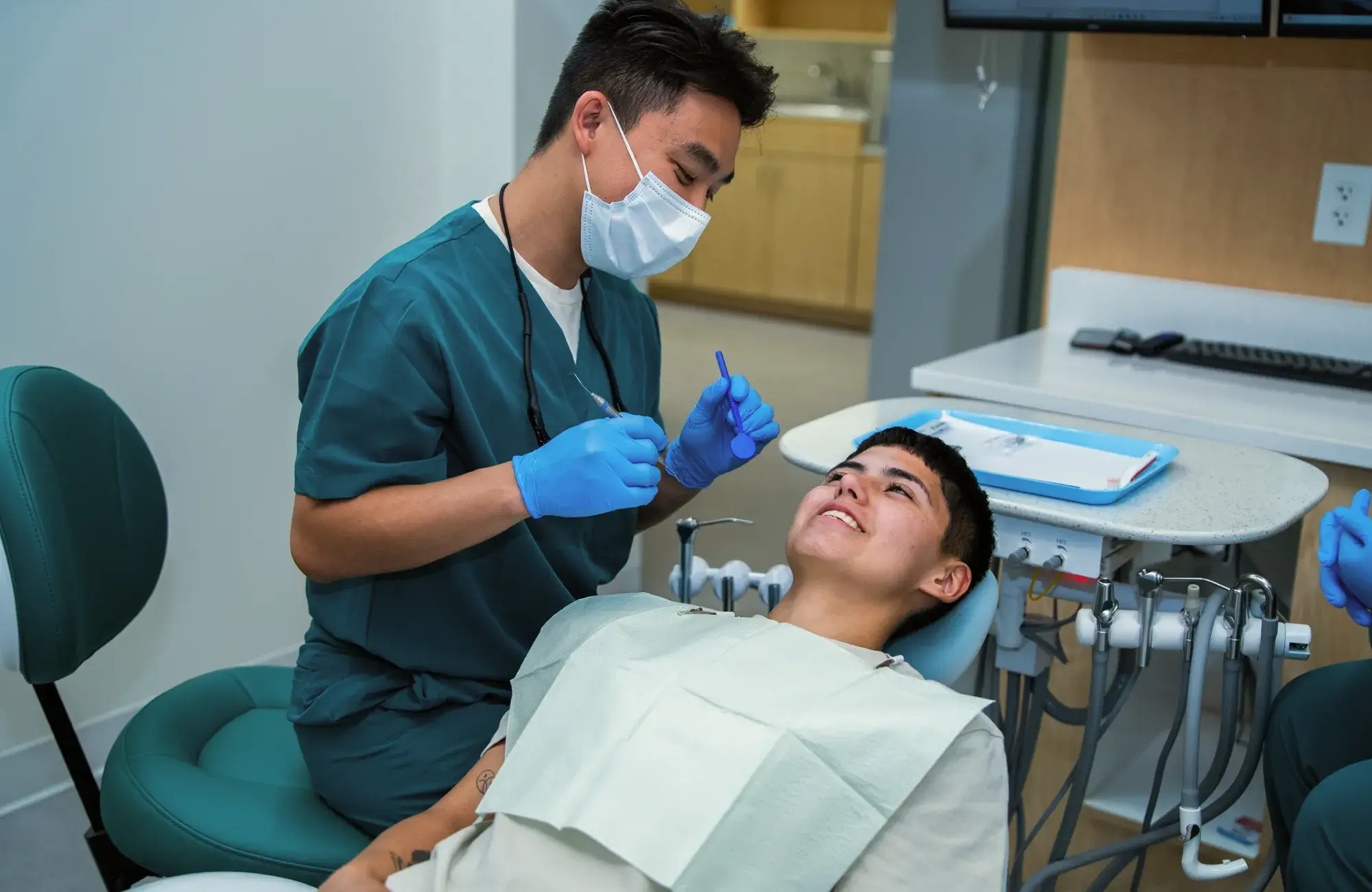 Dentist in blue scrubs examines a patient's teeth in a dental office.