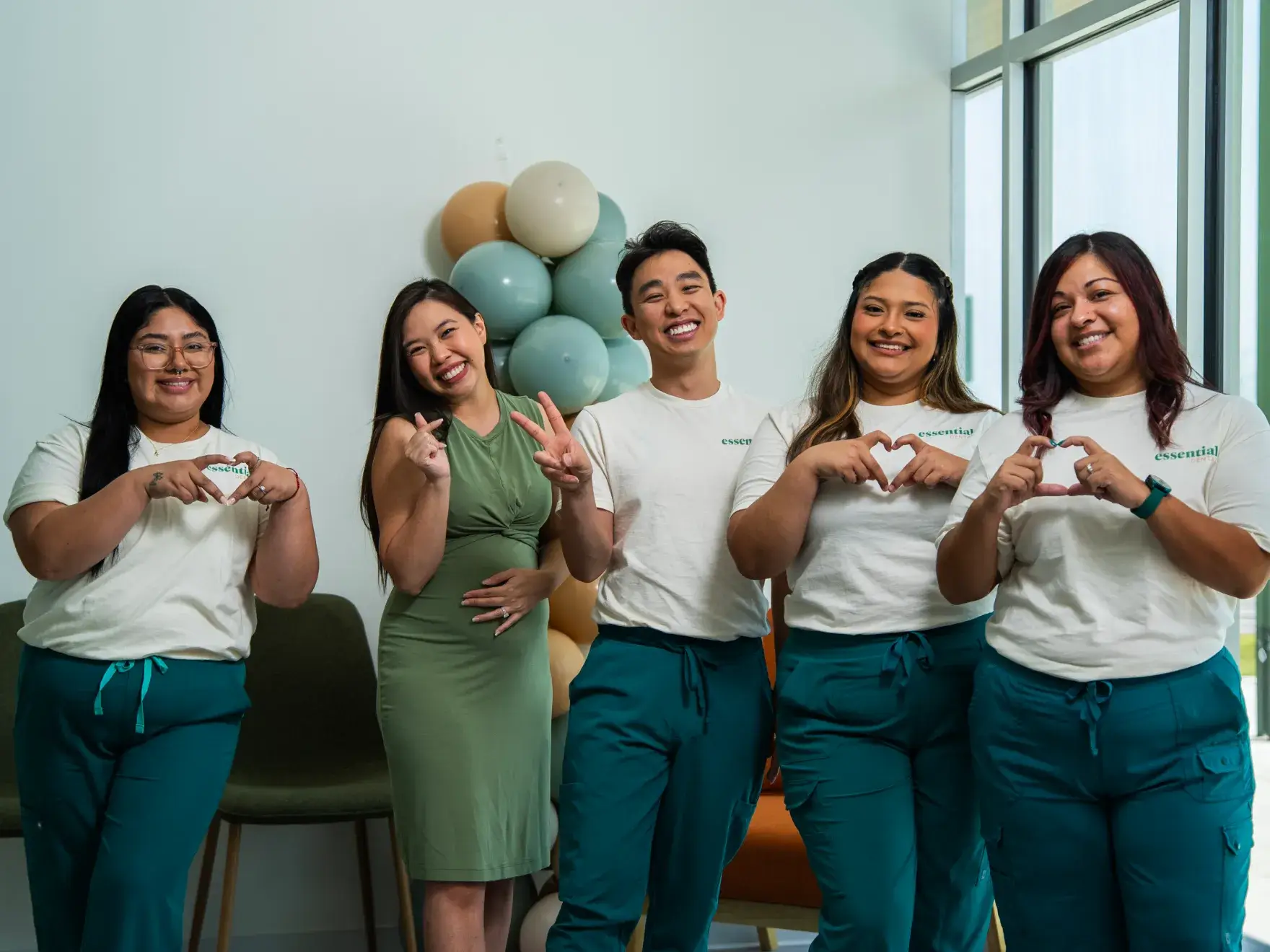 A group of five people smiling and making heart or peace signs with their hands.