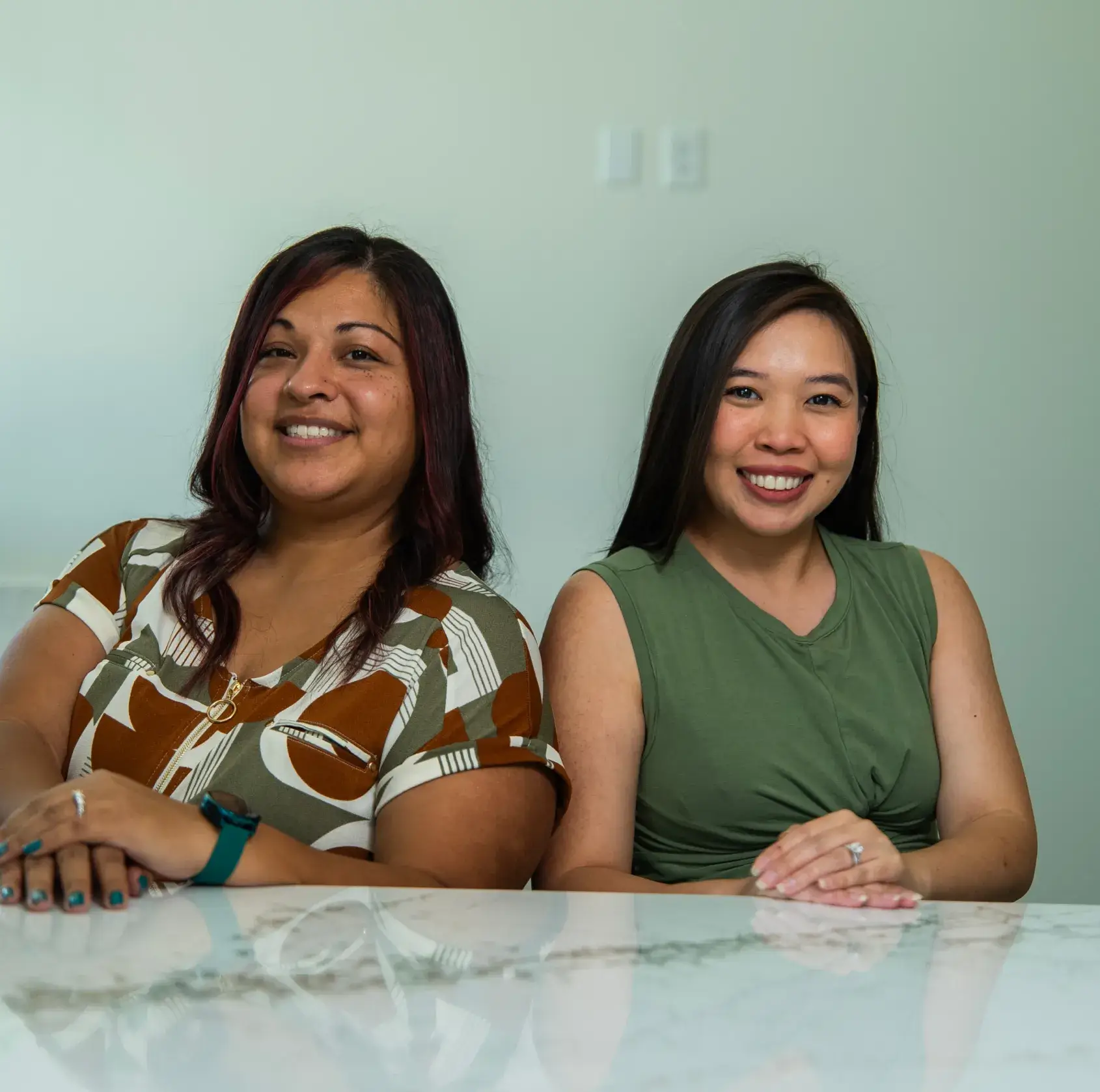 Two women sitting at a table, smiling at the camera in a bright room.
