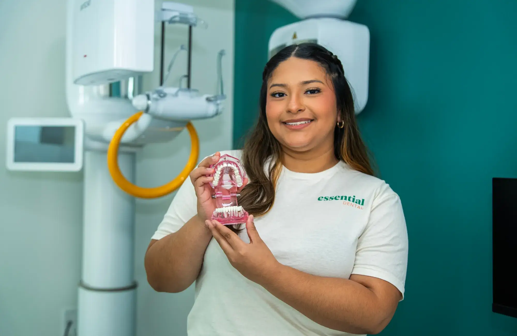 A woman holds a dental model, smiling, in a dentist's office.