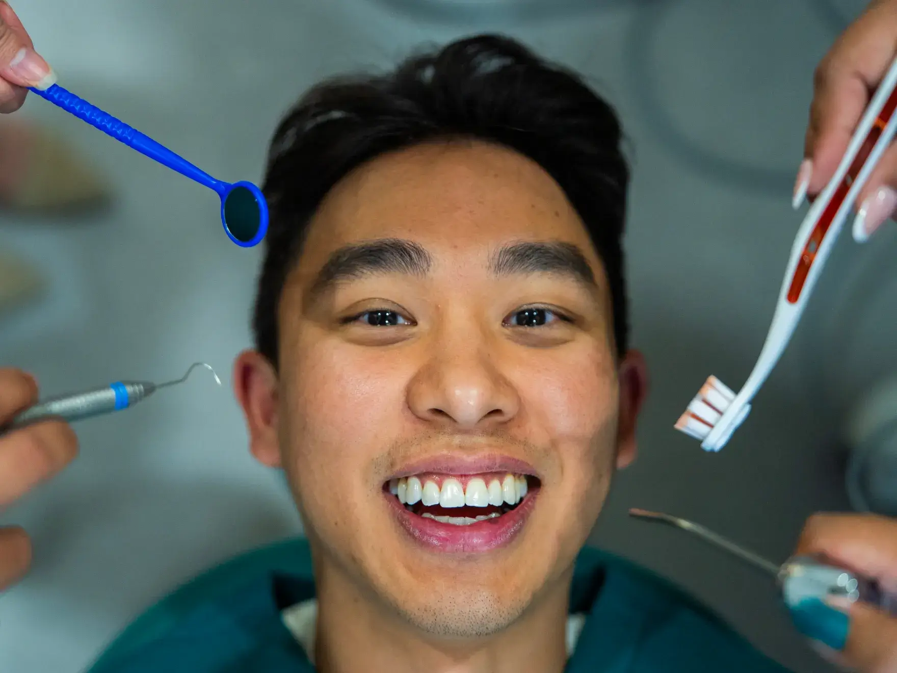 A person is smiling at the dentist with various dental tools surrounding their face.