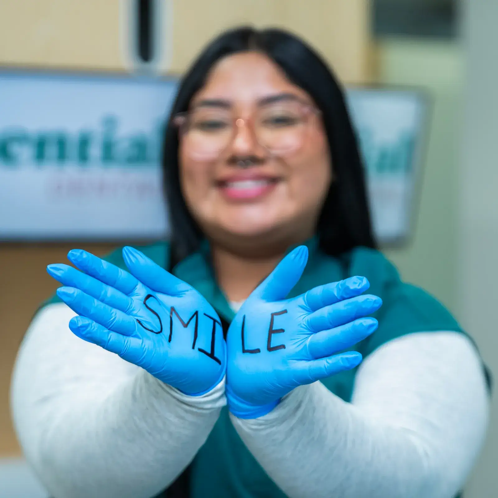 A person wearing blue gloves with "SMILE" written on them holds hands together, smiling.