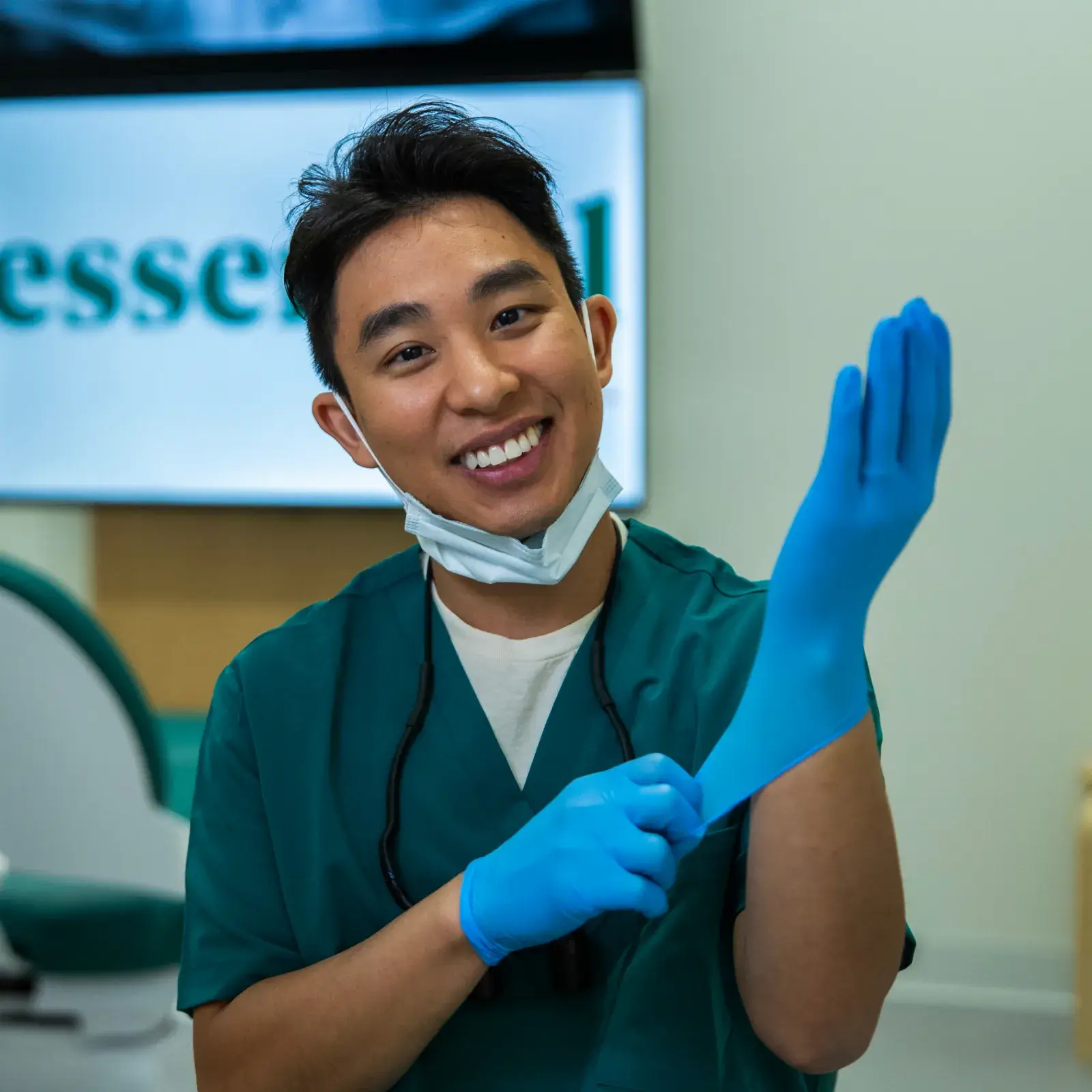 A dentist smiles while putting on a blue glove in a dental office.