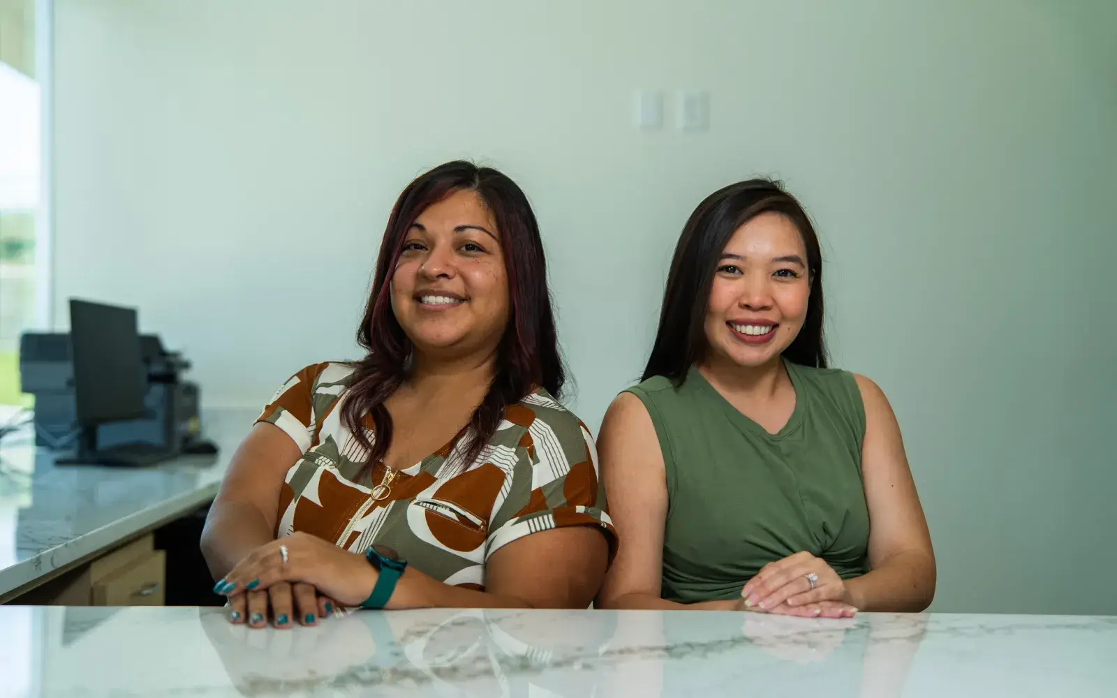 Two women smiling while sitting at a table in an office setting.