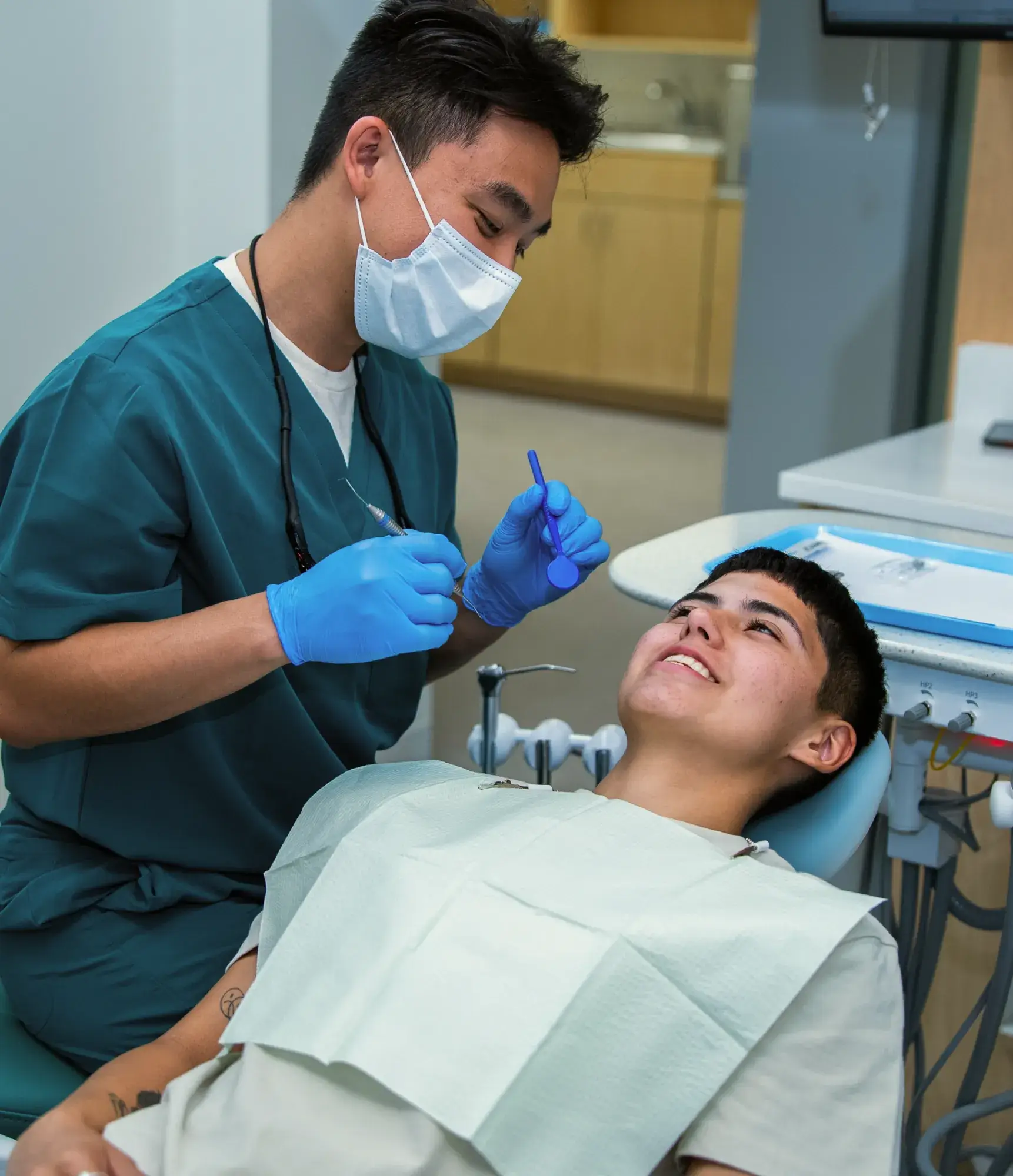 Dentist wearing gloves and mask checks a patient's teeth in a dental office.
