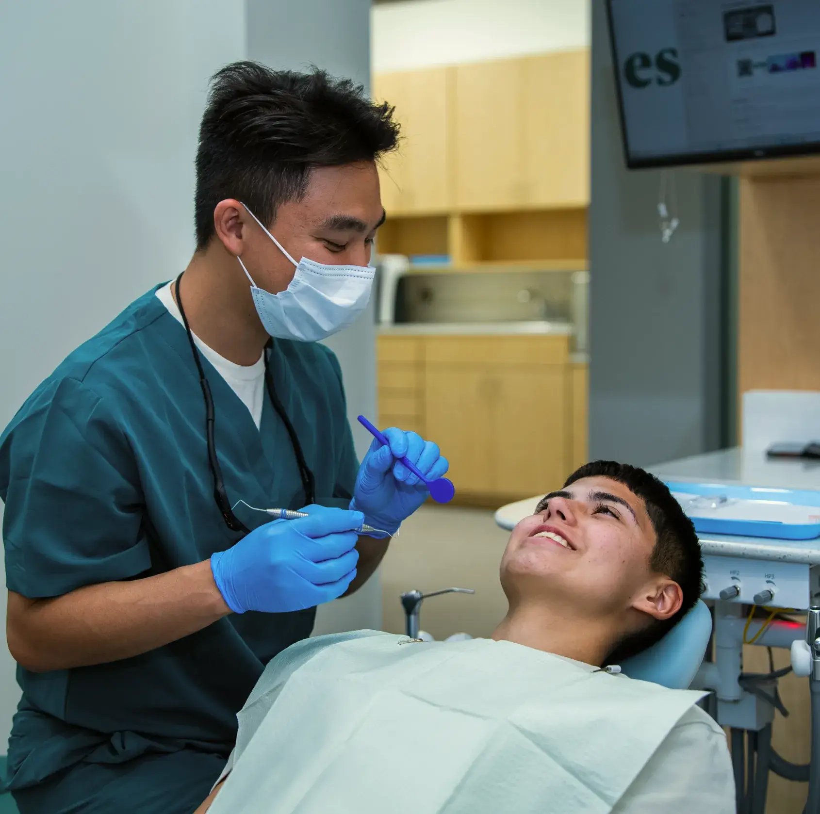 Dentist wearing a mask examines a patient who is lying back in a dental chair.