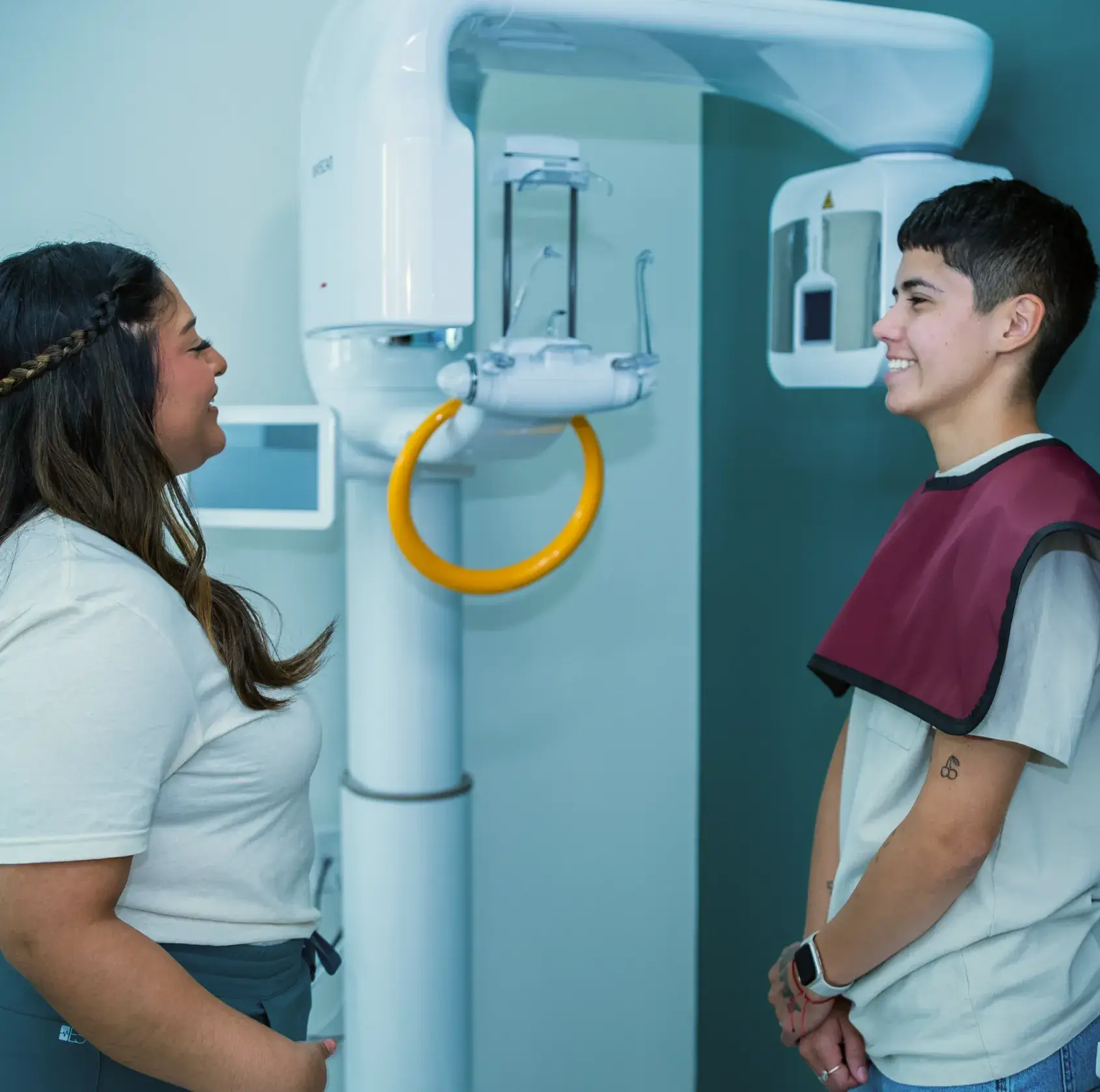 Healthcare professional prepares a patient for a dental X-ray using a large imaging machine.