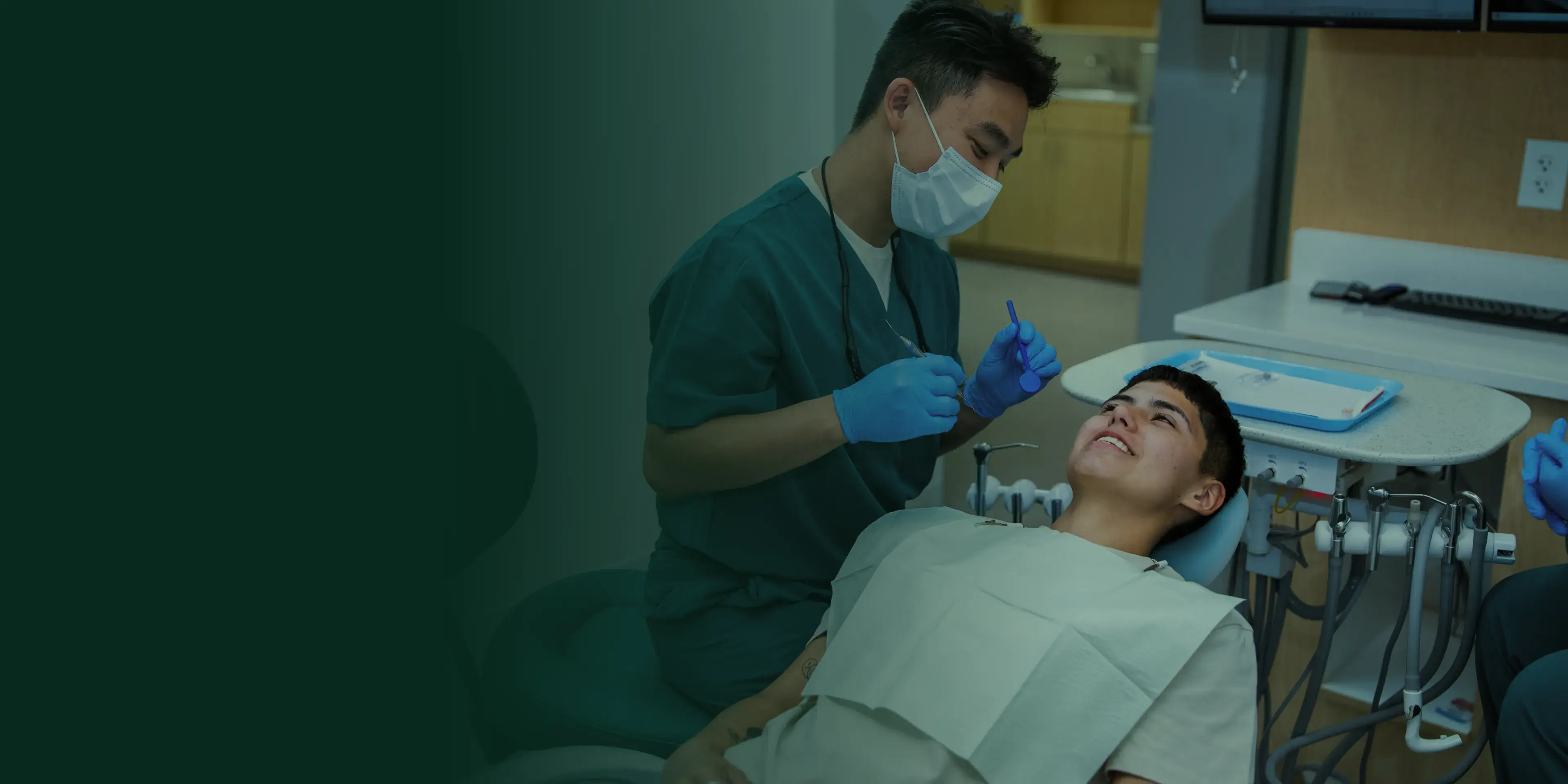 A dentist wearing a mask examines a smiling patient in a dental chair.