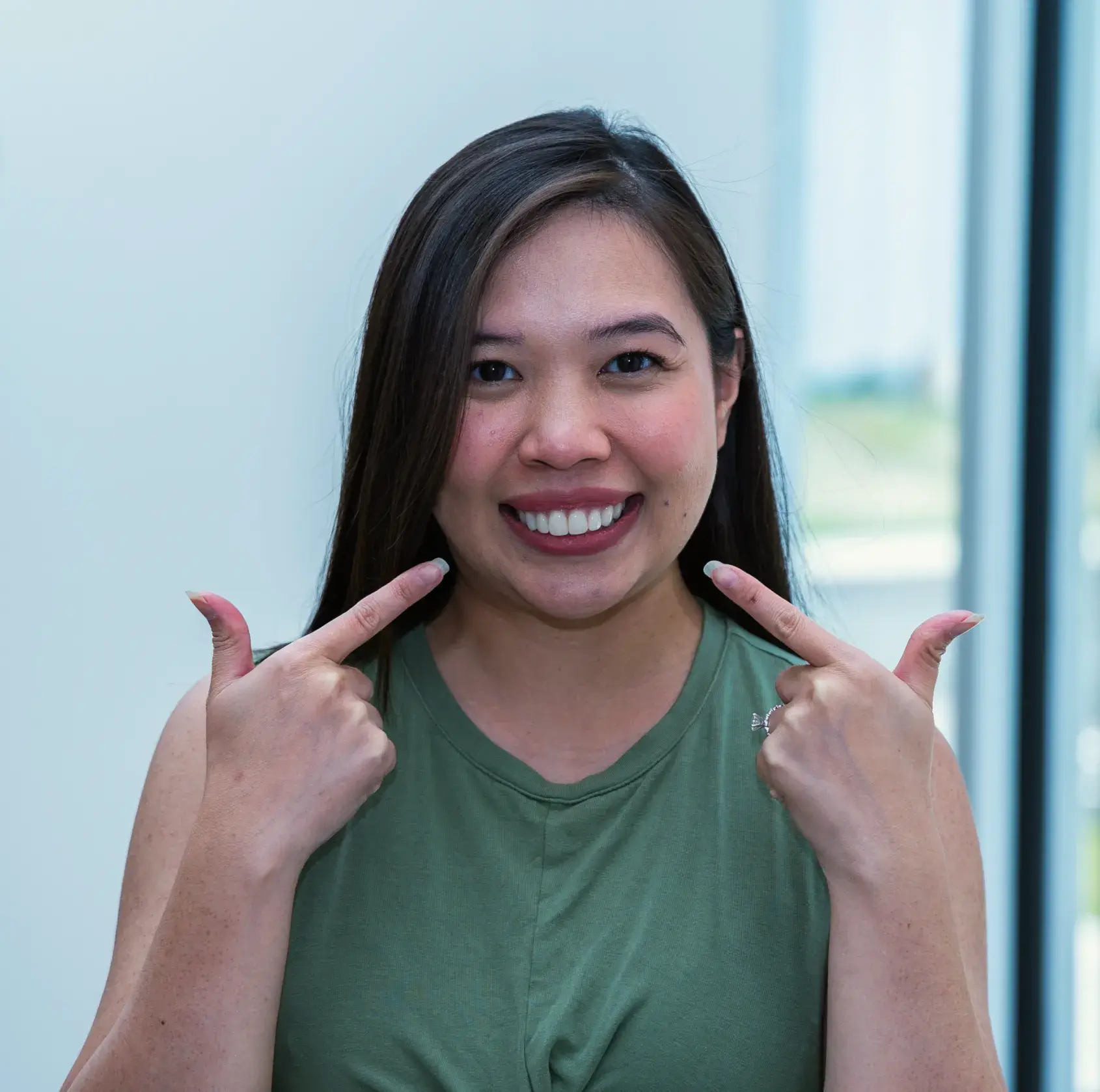 A woman in a green shirt smiling and pointing at her teeth.