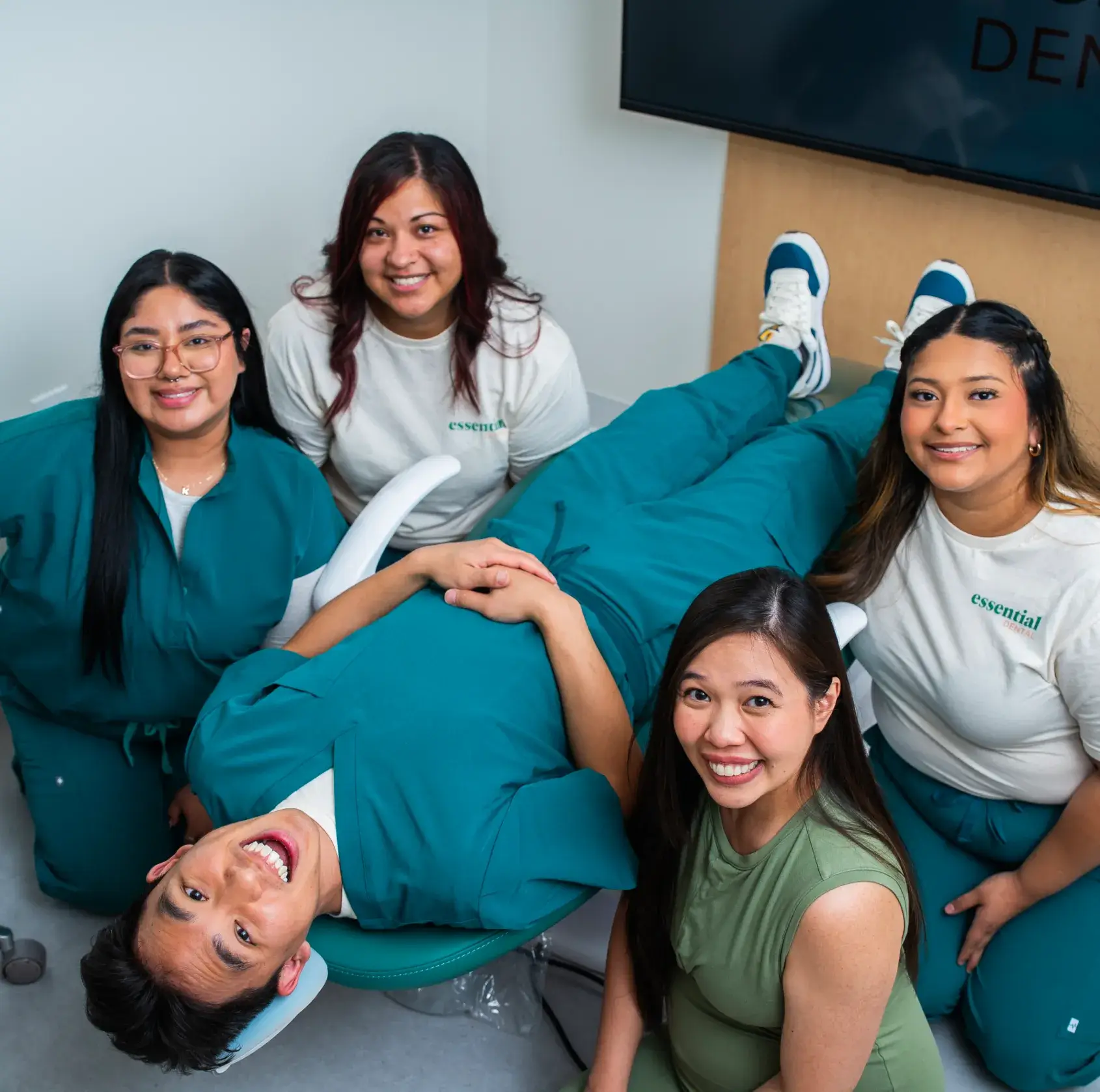 A person lies on a dental chair smiling, surrounded by four people standing around.