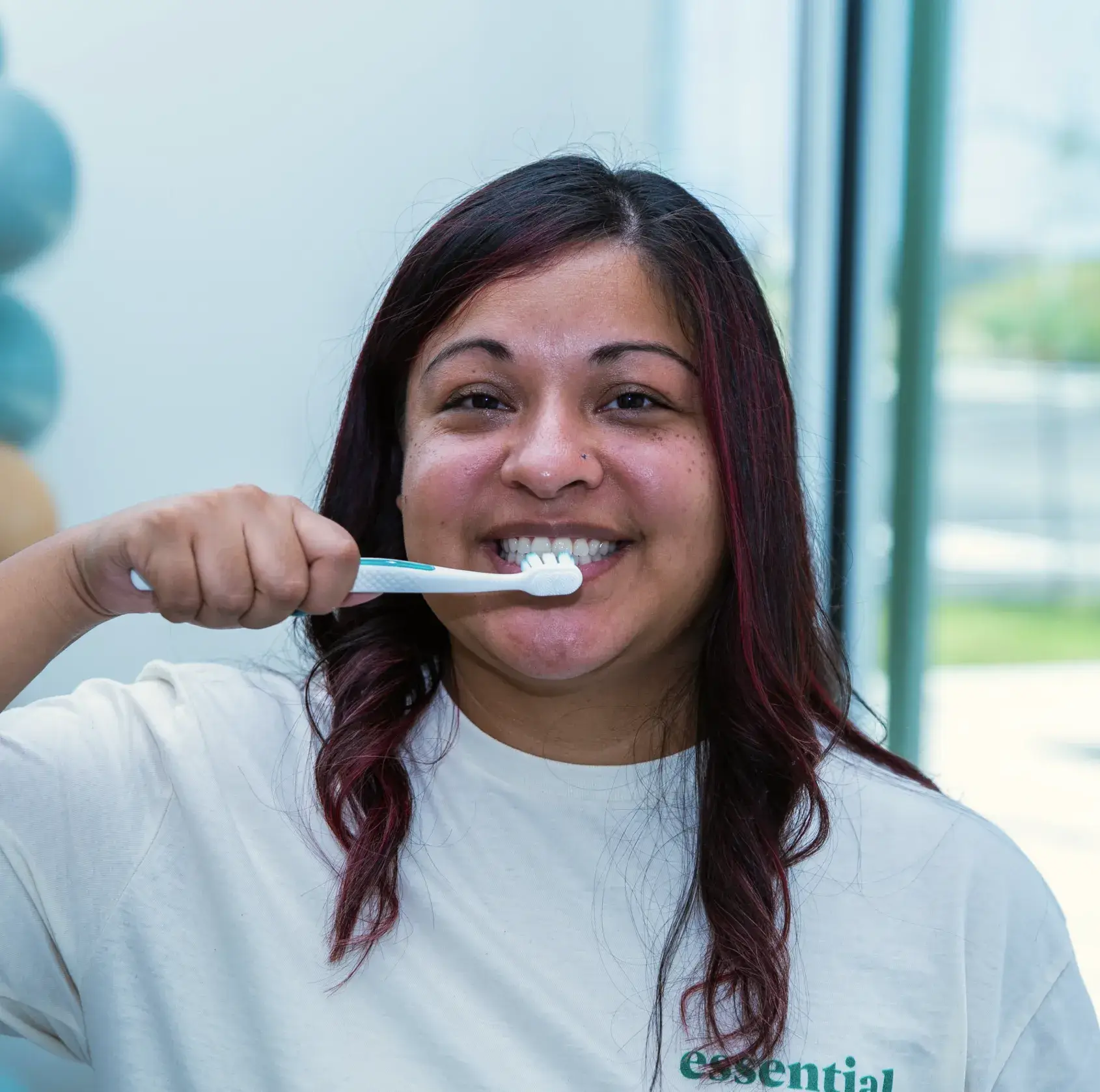 A person smiling while brushing their teeth with a white toothbrush.