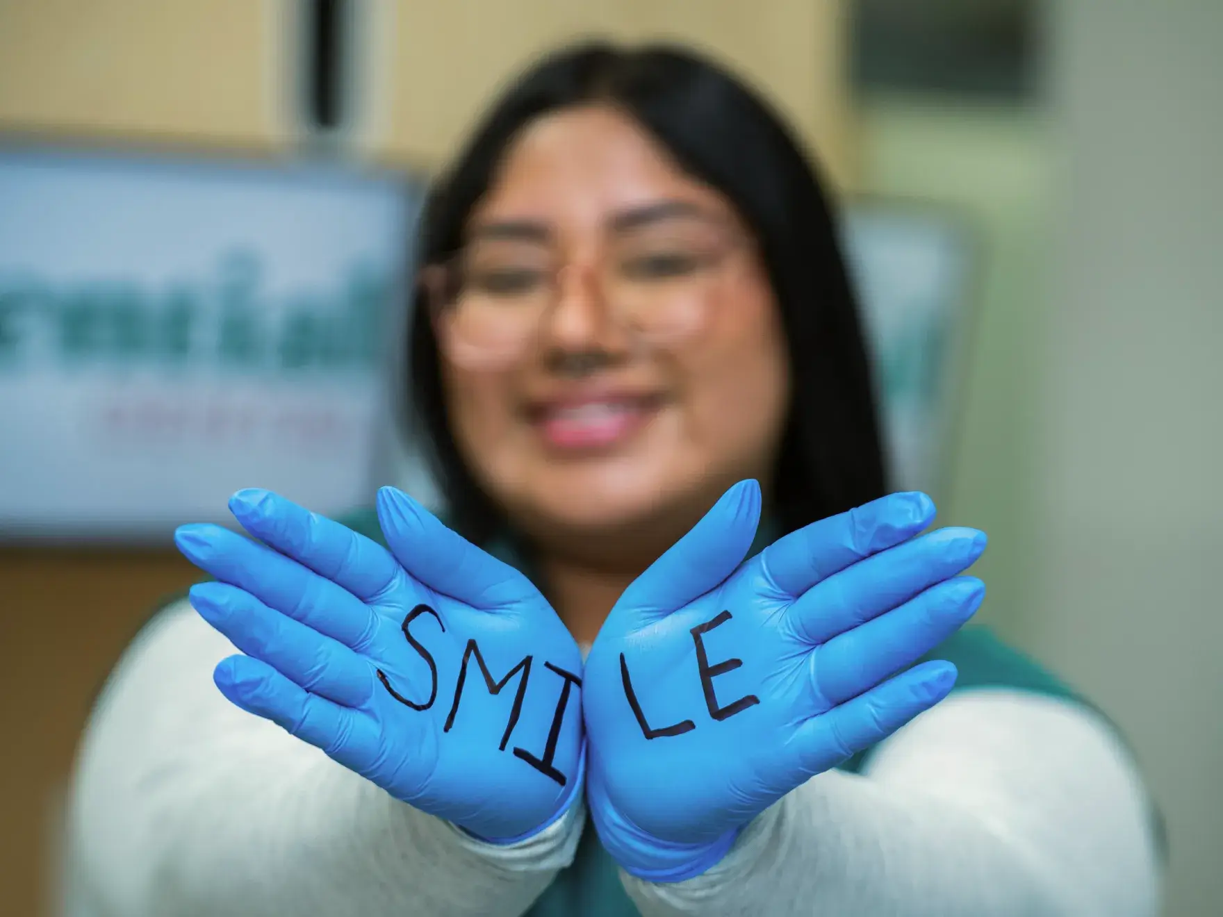 A person wearing gloves with "SMILE" written on them holds their hands together, smiling in the background.