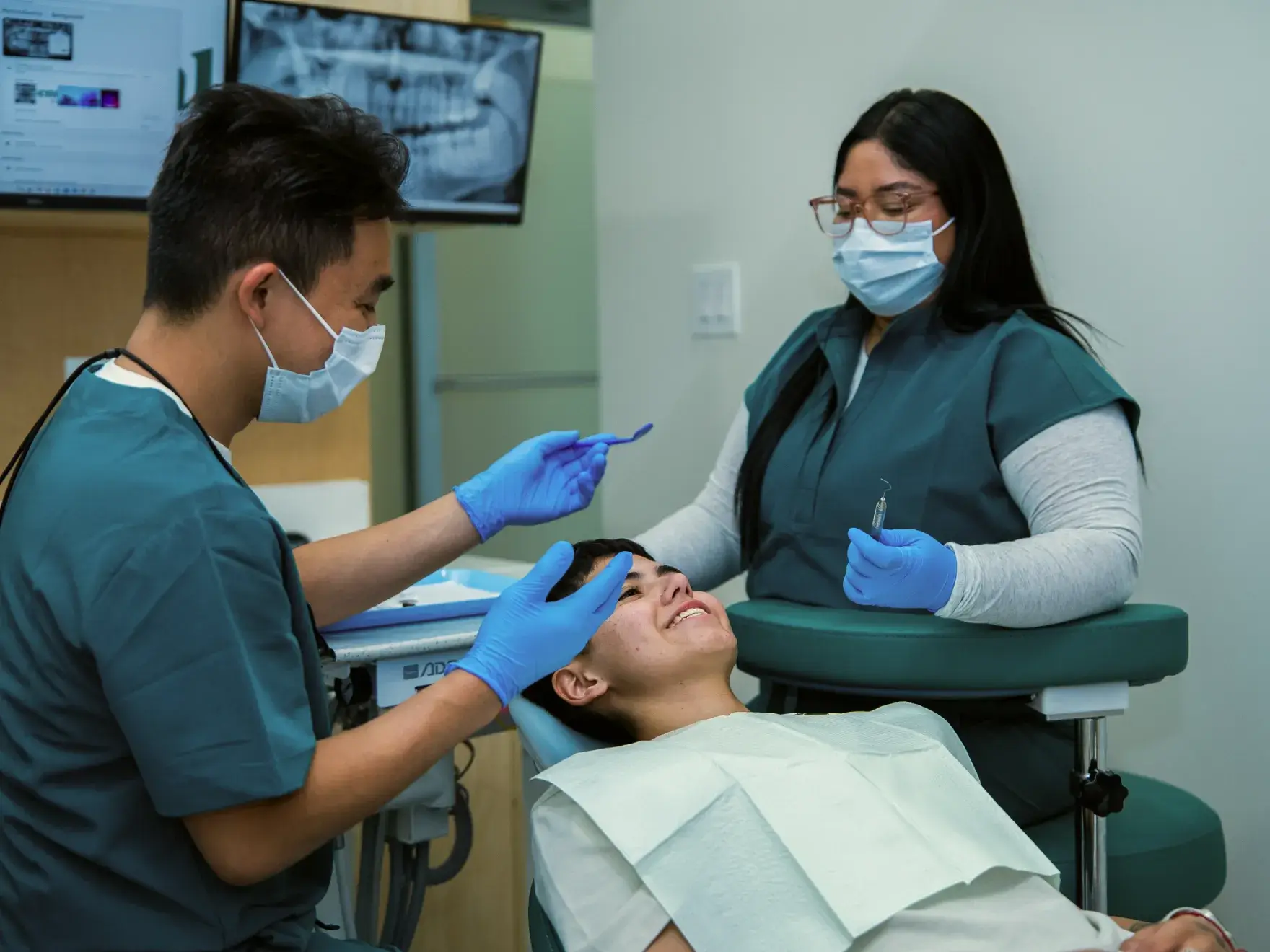 A dentist and dental assistant examine a patient lying in a dental chair.