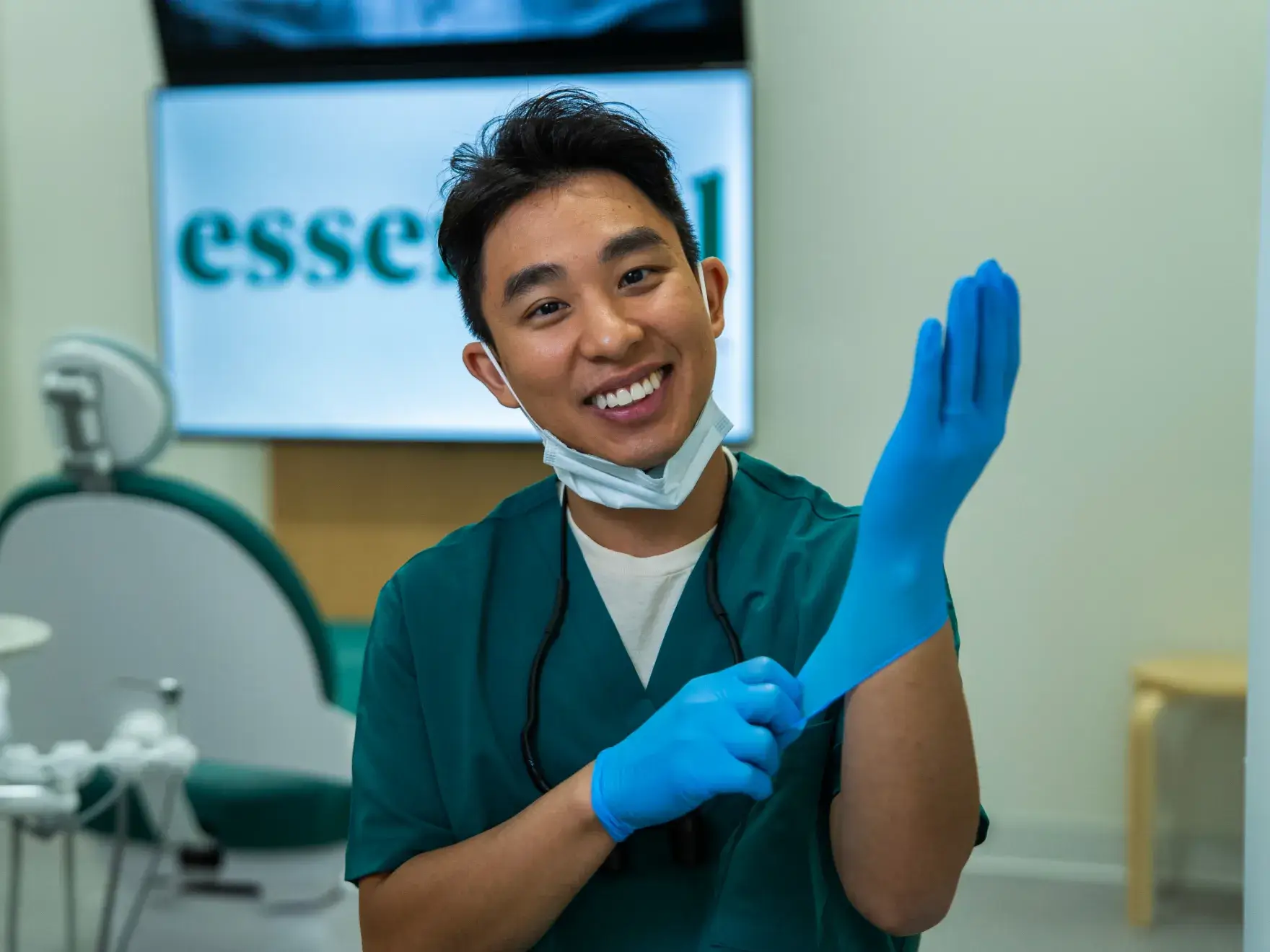 A dentist putting on blue gloves smiles while preparing for work in a dental office.